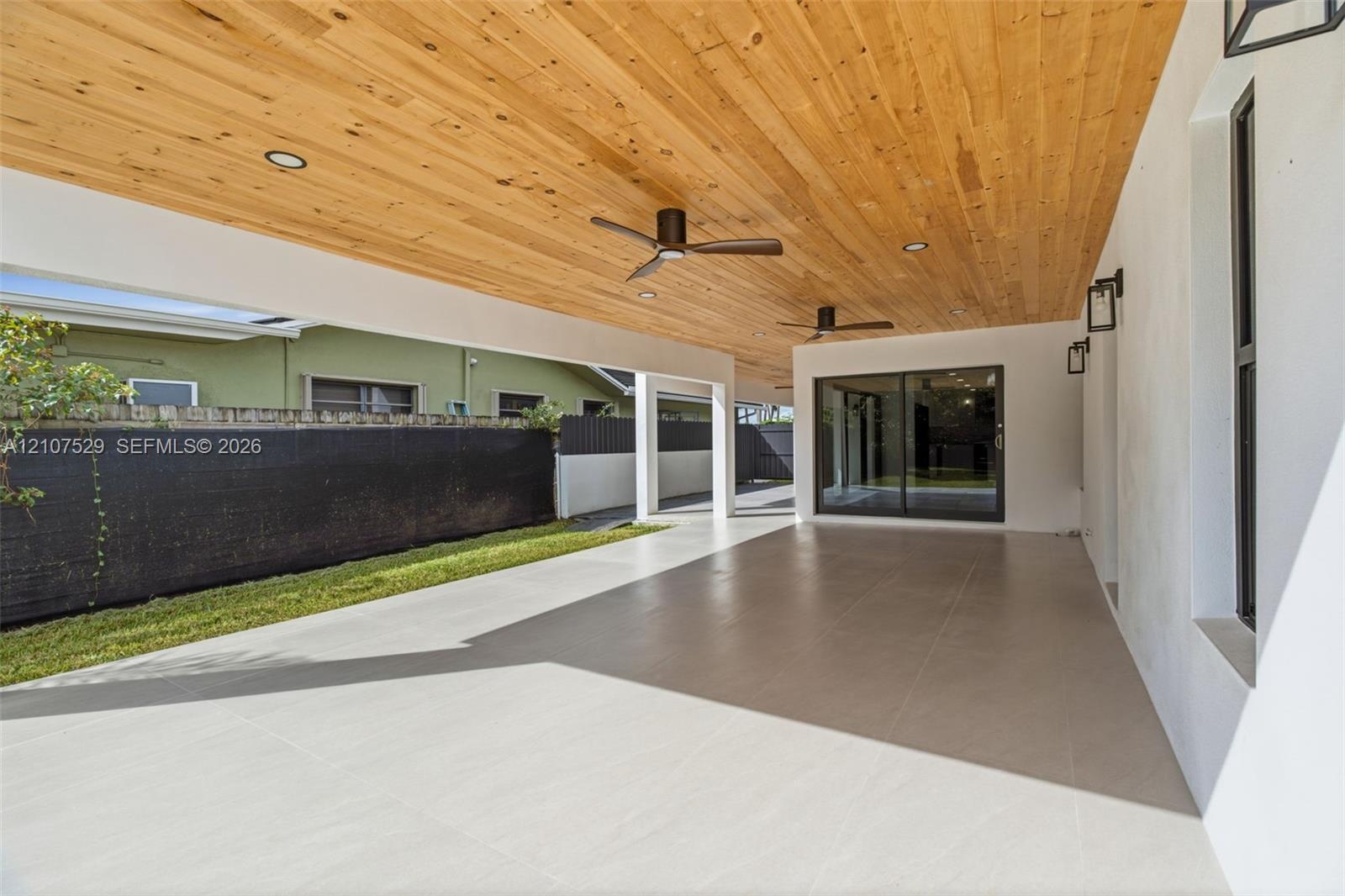 Covered patio featuring a wood-plank ceiling, ceiling fan, large sliding glass doors, and light-toned tile flooring