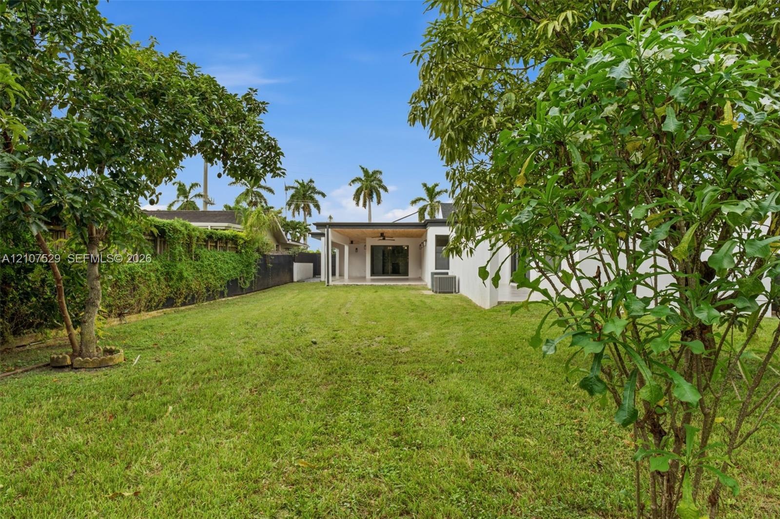 Expansive backyard featuring a large grass lawn, mature trees, and perimeter fencing