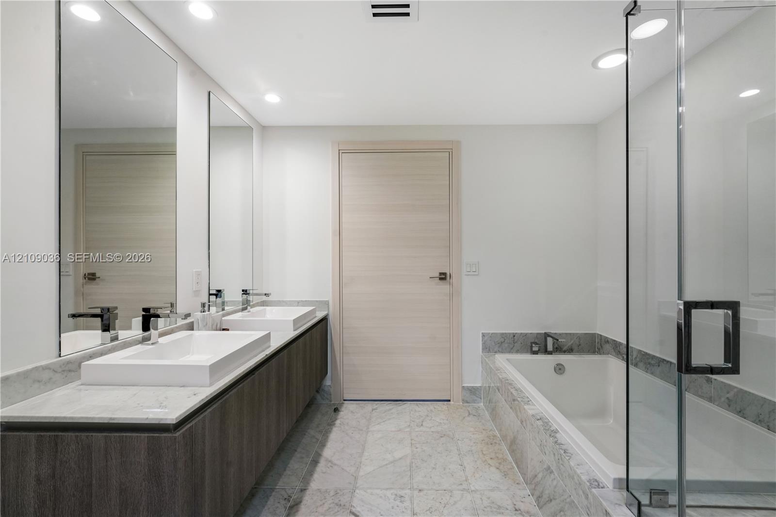 Floating double vanity with dual rectangular vessel sinks, stone-surface countertop, floor-to-ceiling mirrors, recessed lighting, and a glass-enclosed