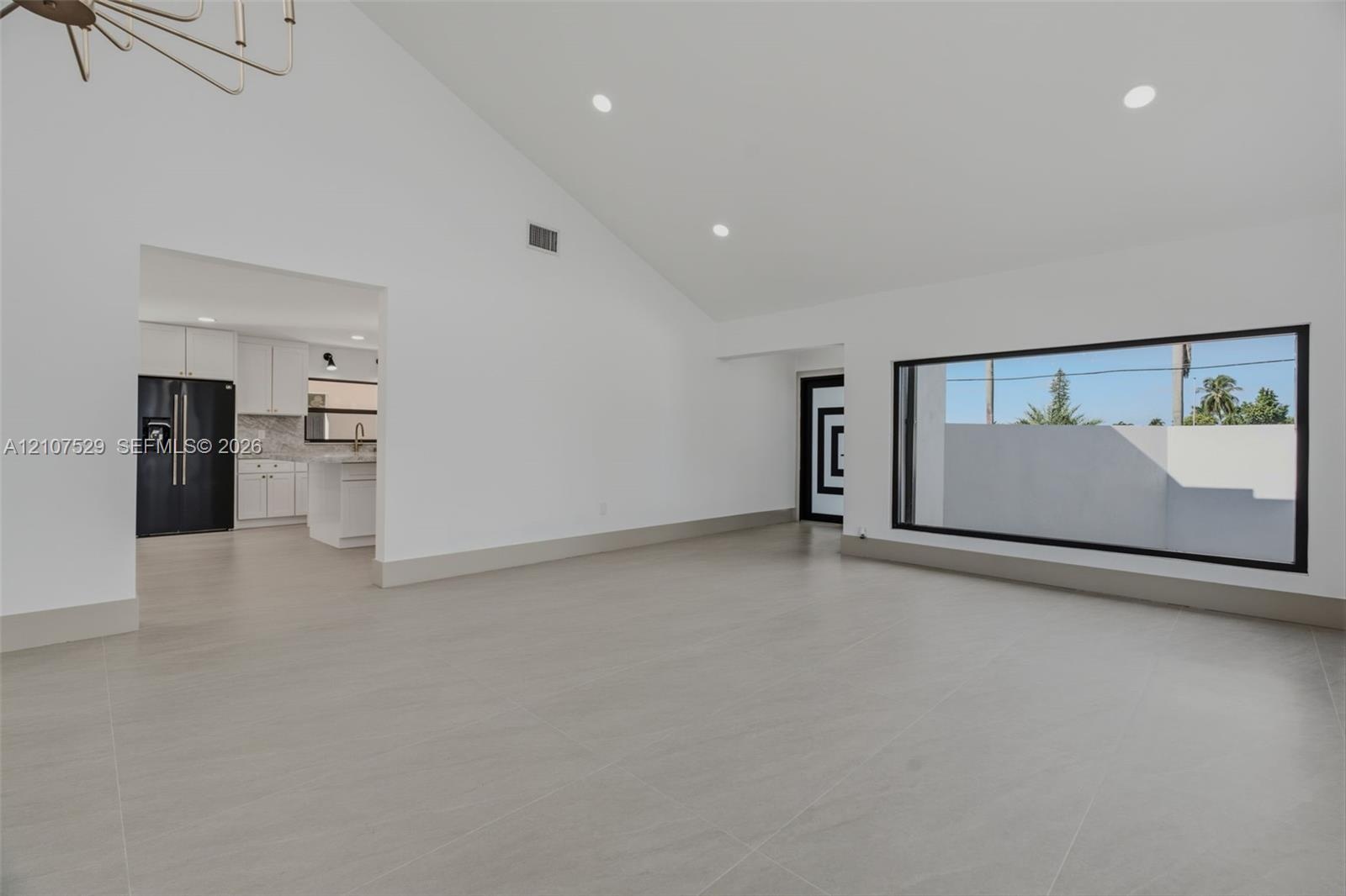 Vaulted ceilings featuring recessed lighting and a multi-arm chandelier, large-format tile flooring, oversized picture windows, and double-entry doors
