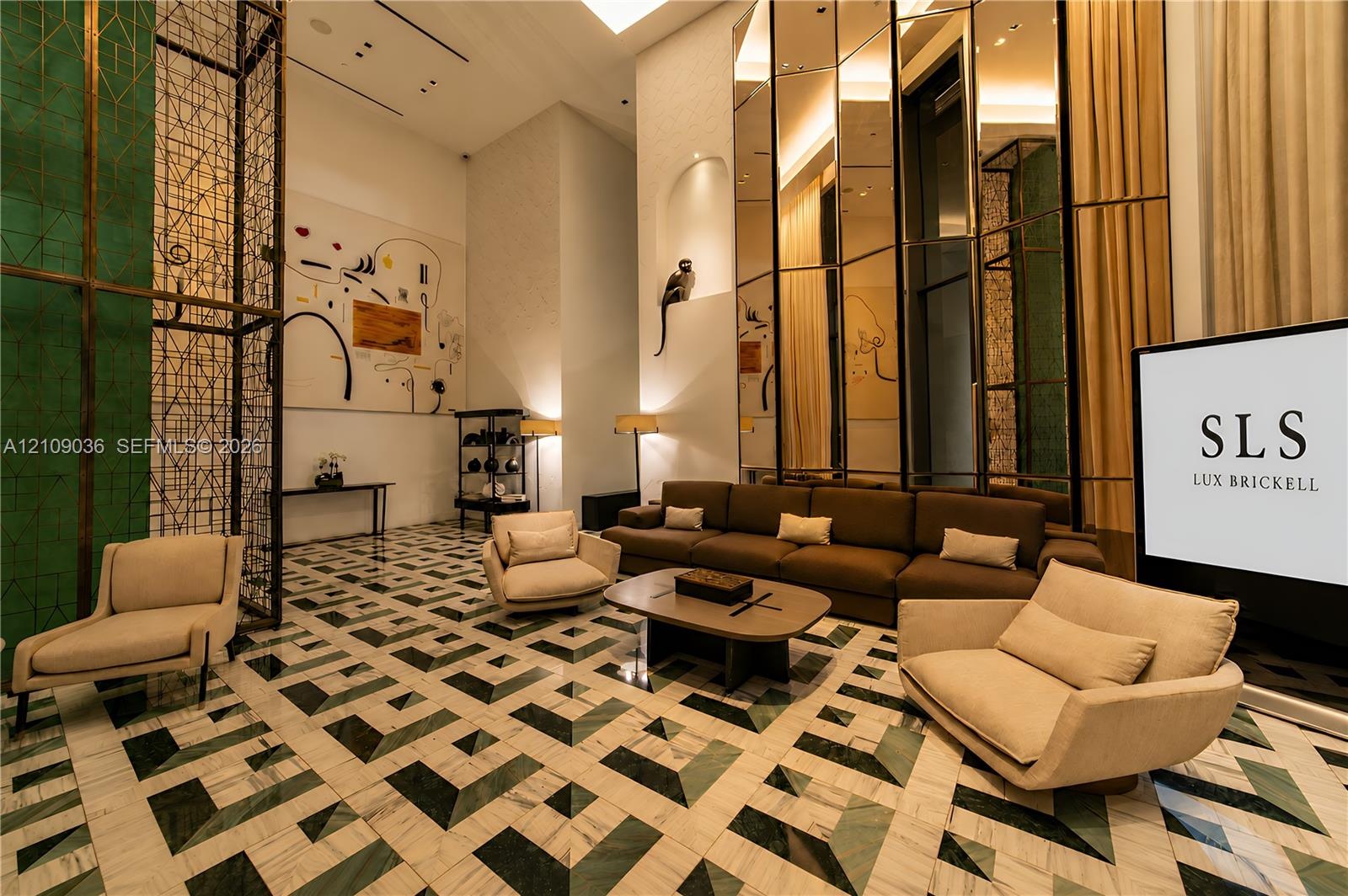 Double-height lobby featuring geometric patterned stone flooring, floor-to-ceiling mirrored paneling, and an intricate metal privacy screen