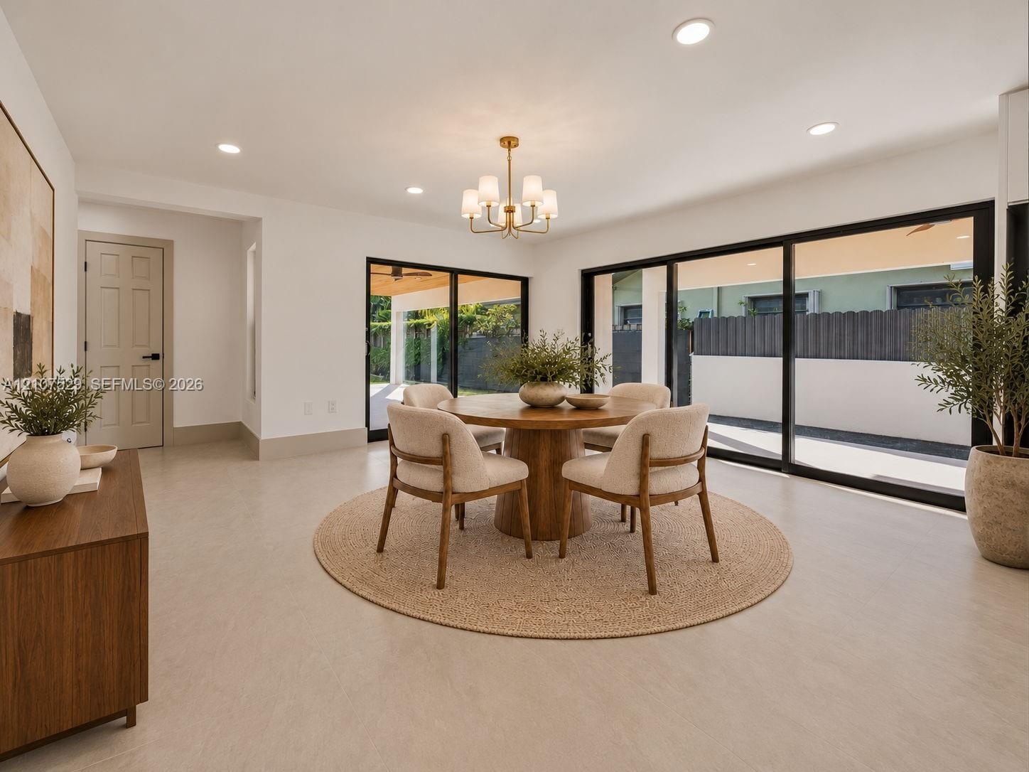 Open-concept interior featuring a center island with quartz countertops, custom white cabinetry, recessed lighting, multi-arm chandeliers, and large-f