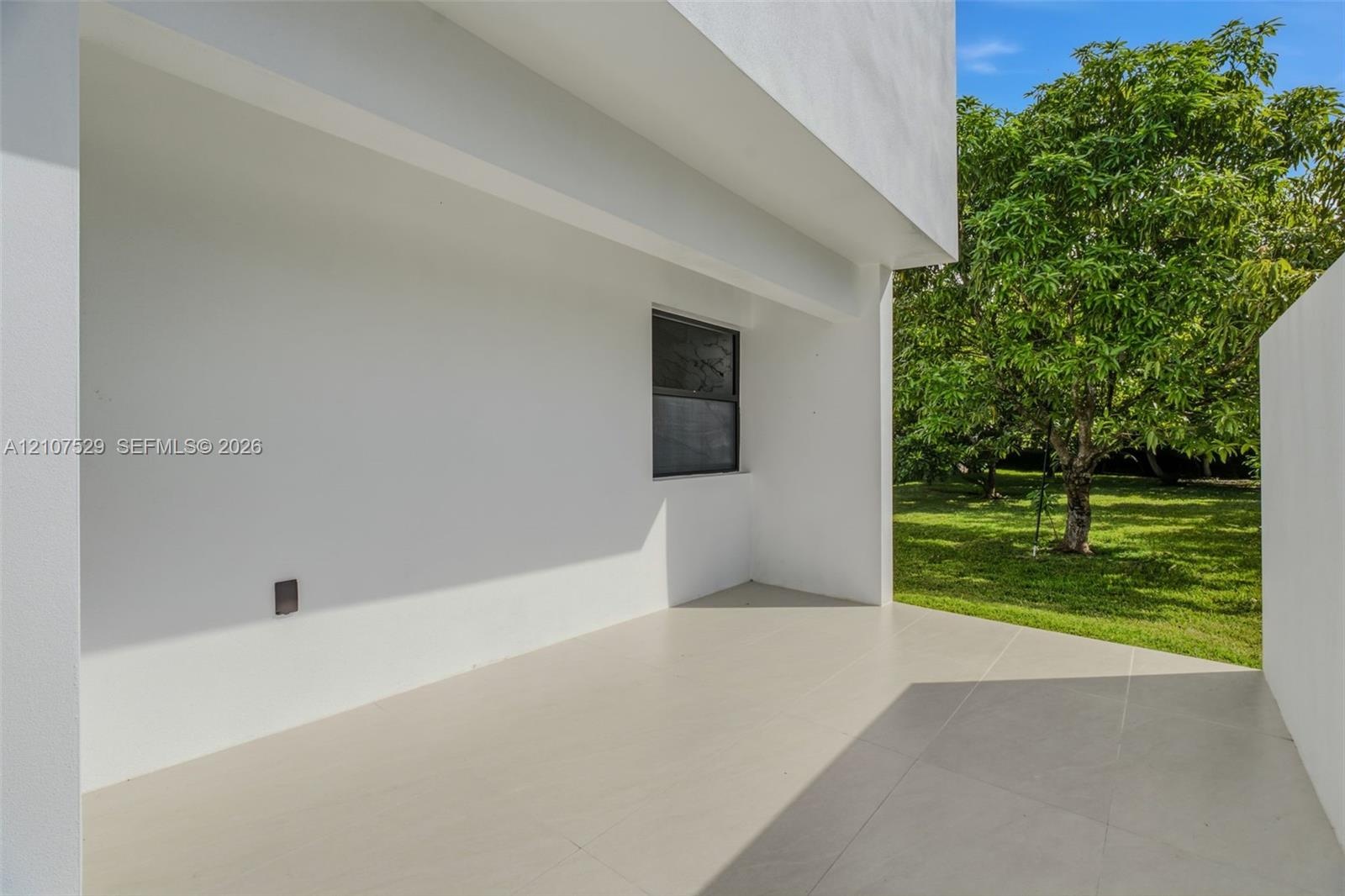 Modern exterior patio featuring large-format porcelain tile flooring, expansive floor-to-ceiling sliding glass panels, smooth white stucco finish, and