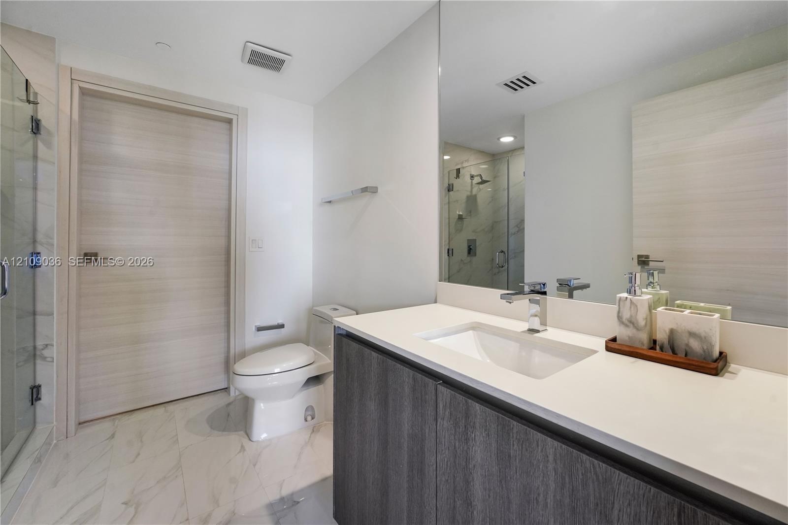 Modern vanity with a light-toned countertop, integrated basin, and dark wood-finish cabinetry, paired with large-format stone-finish floor tile, a ful