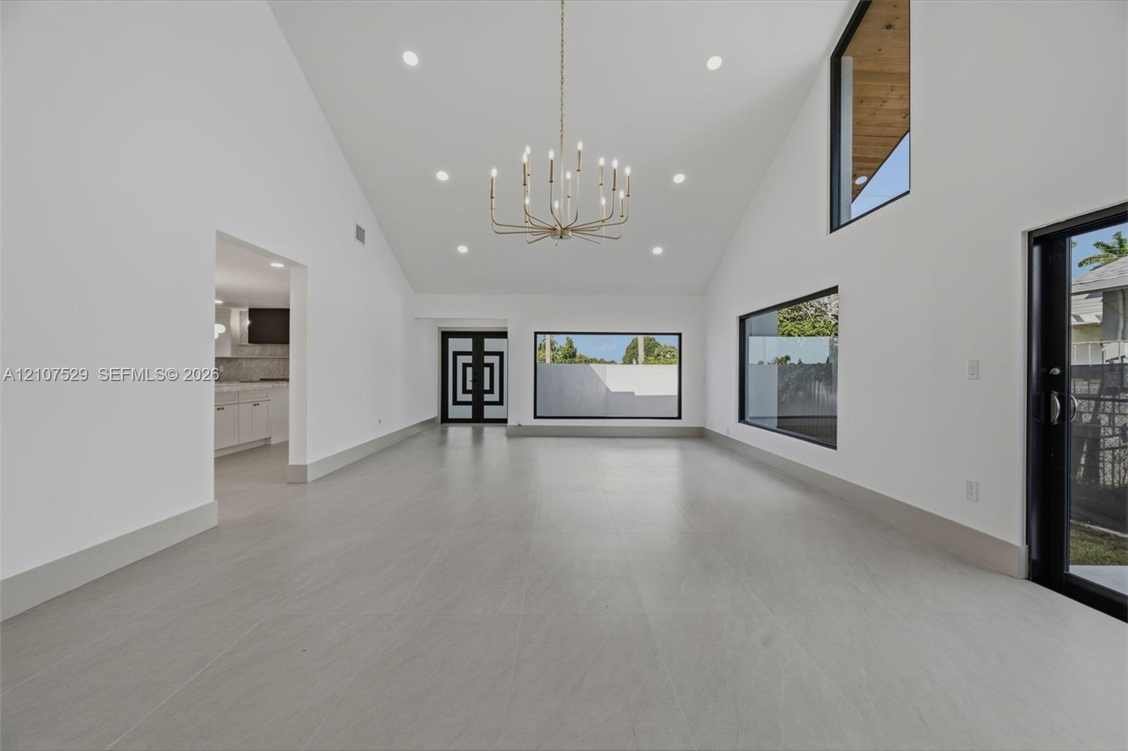 Neutral-toned interior featuring large-format flooring, recessed lighting, a multi-arm chandelier, and expansive sliding glass doors