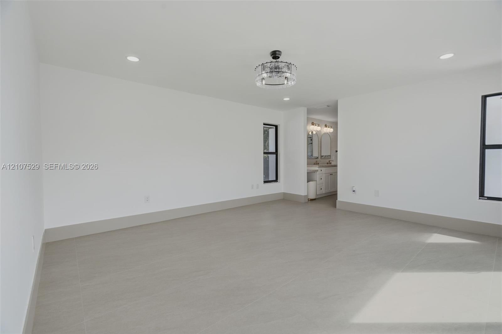 Minimalist interior featuring large-format tile flooring, recessed lighting, a modern drum-style chandelier, and expansive sliding glass doors framed 