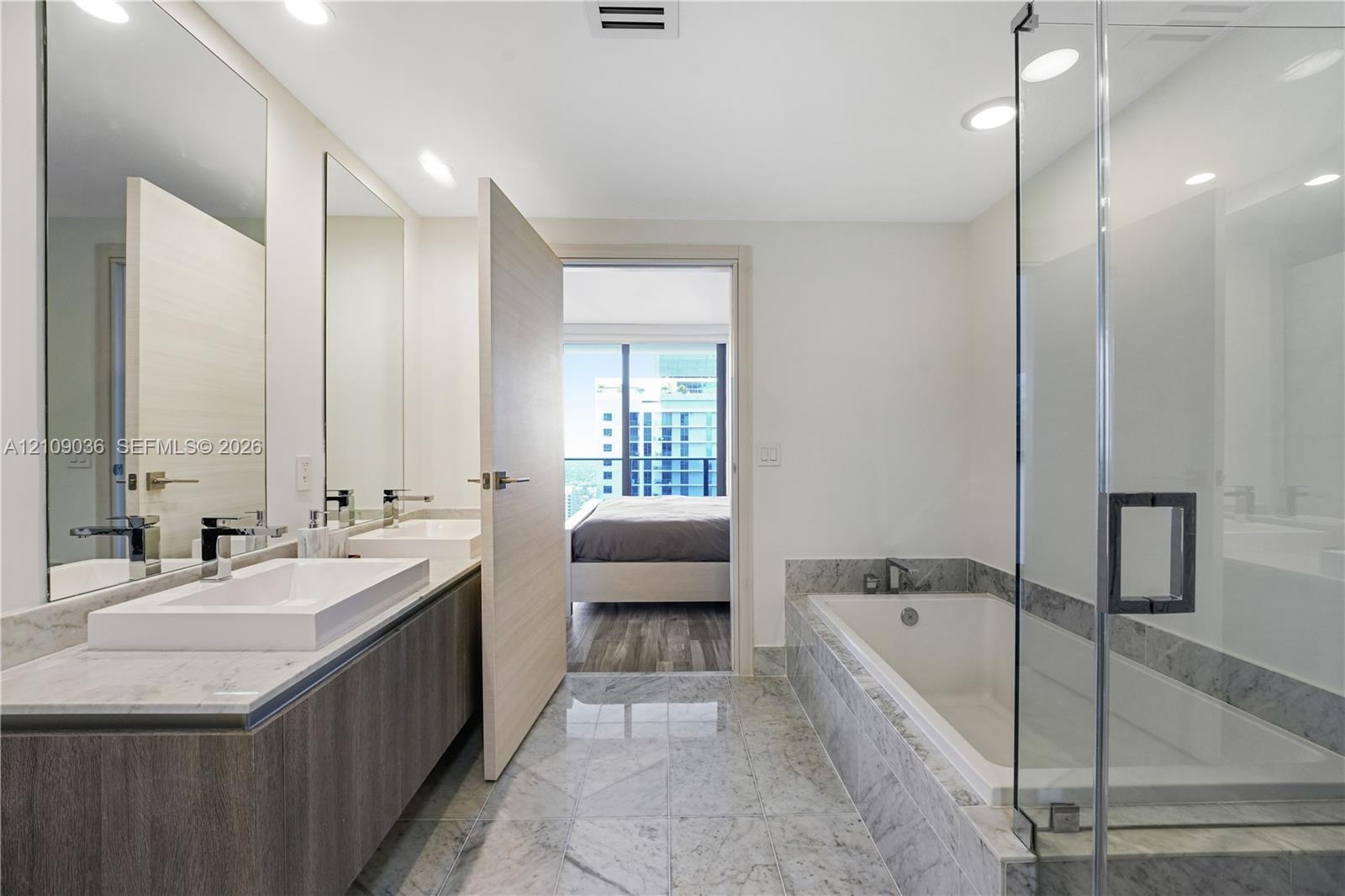 Double vanity featuring rectangular vessel sinks and stone-surround countertop, stone tile flooring, deep soaking tub, and a glass-enclosed shower
