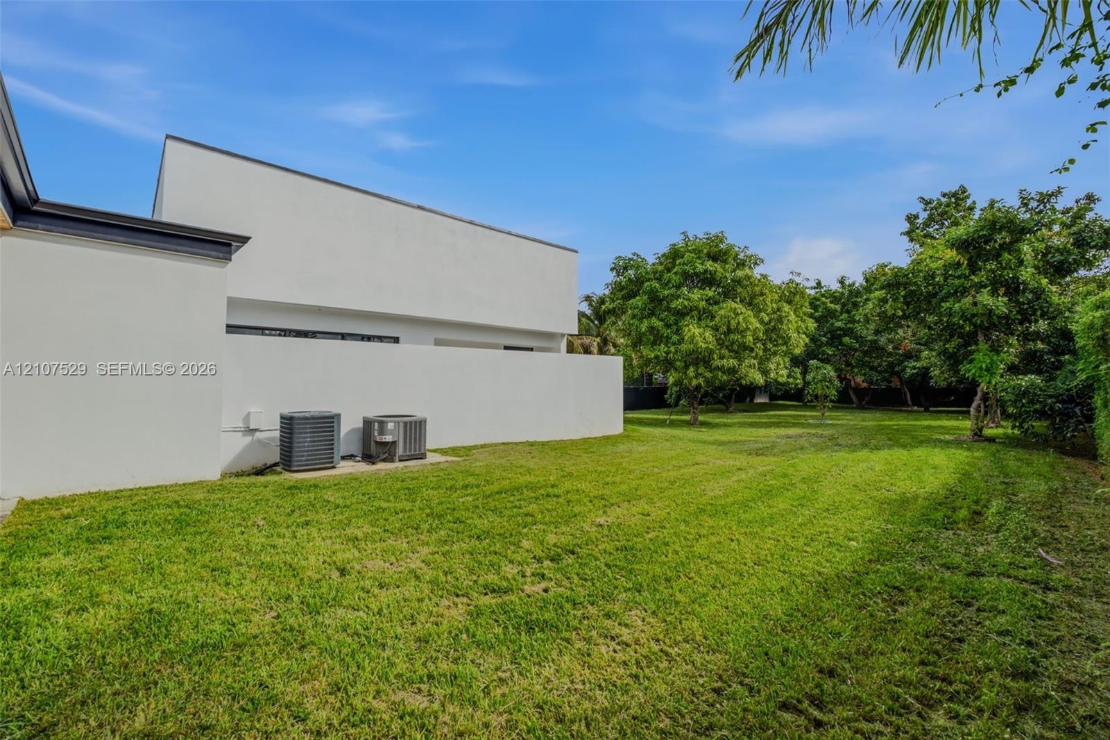 Modern exterior with a smooth white stucco finish, expansive manicured lawn, and a covered outdoor patio featuring wood-paneled ceiling detailing