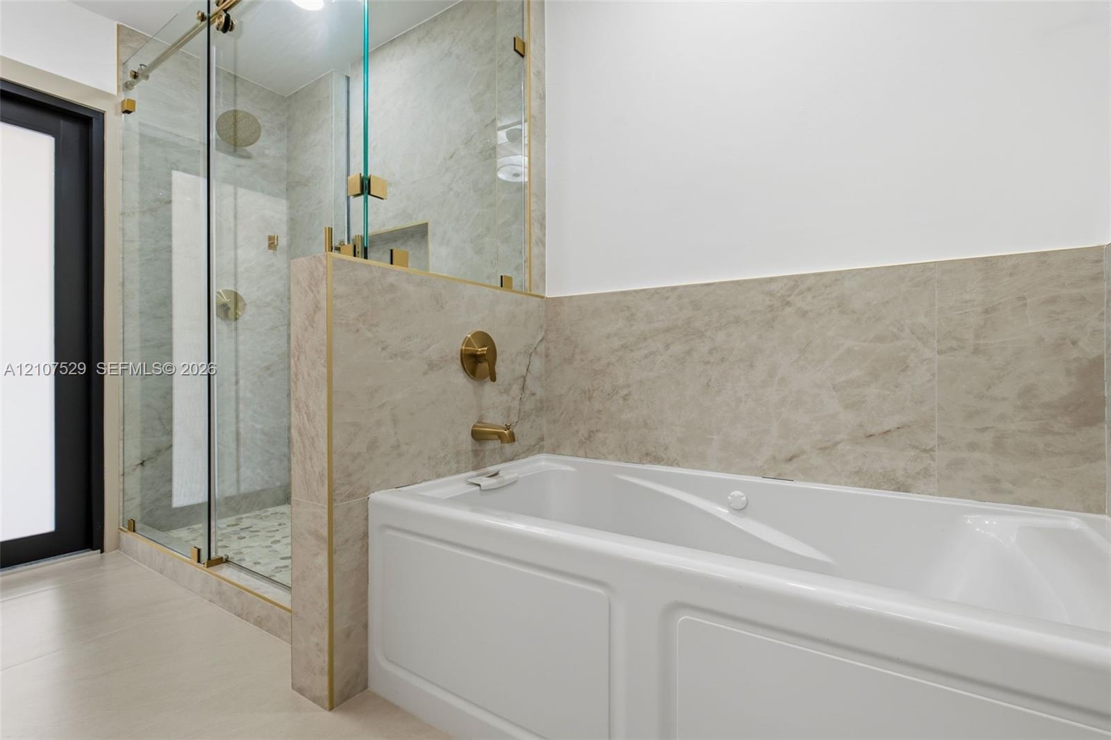 Dual-sink vanity with white cabinetry and stone-finish countertops, glass-enclosed shower with gold-tone hardware, pebble-stone shower flooring, and a