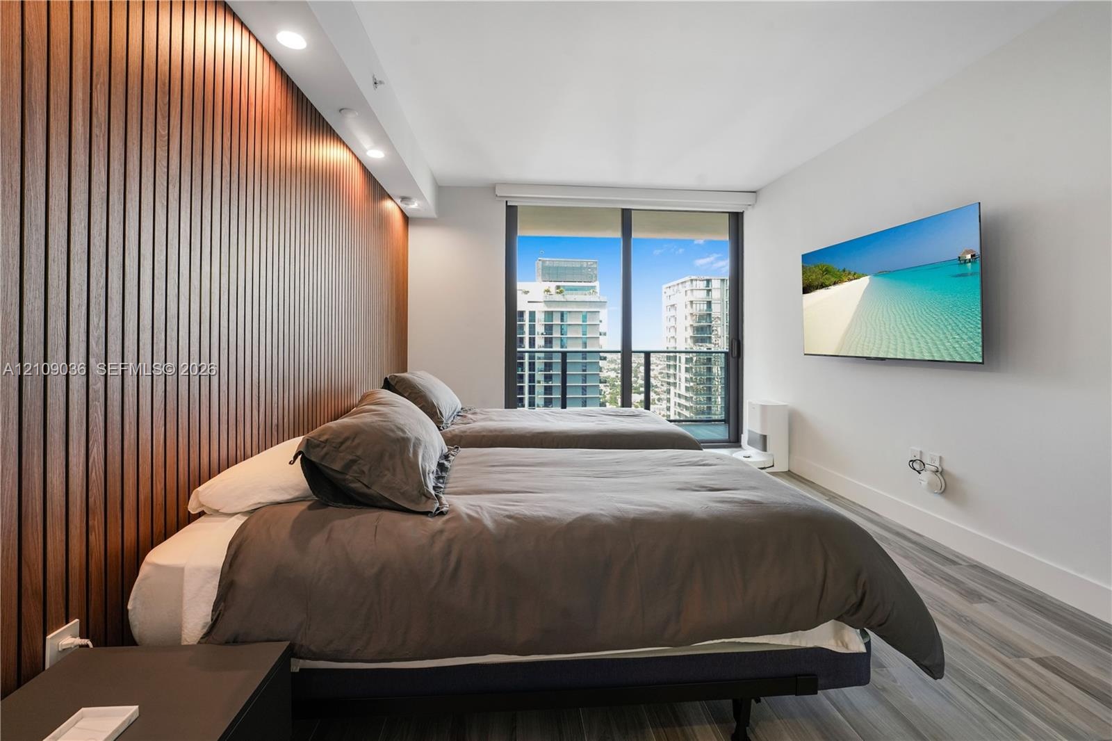 Floor-to-ceiling slatted wood-finish accent wall with integrated recessed lighting, wood-finish flooring, and large-format sliding glass door leading 