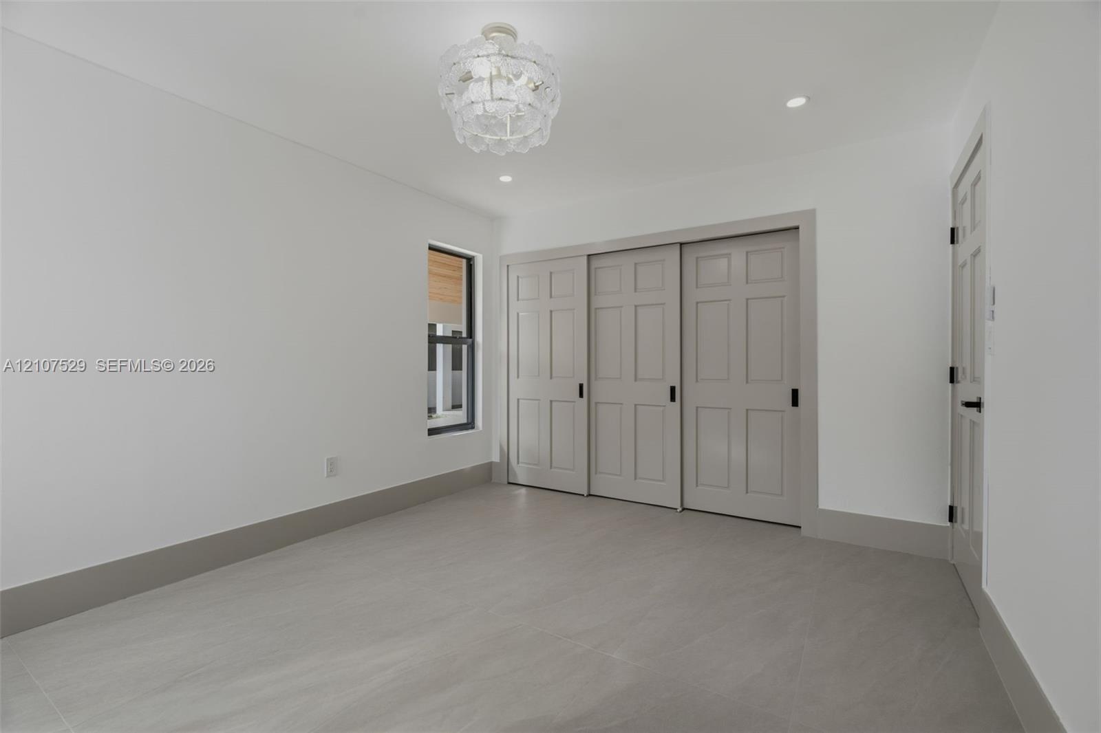Neutral-toned tile flooring, recessed lighting, ornate central pendant fixture, black-framed windows, and built-in closet with panel doors