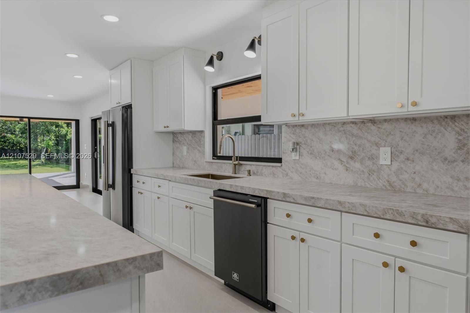 Kitchen featuring white shaker-style cabinetry, a large island with integrated microwave, stone-finish countertops and backsplash, black matte range w