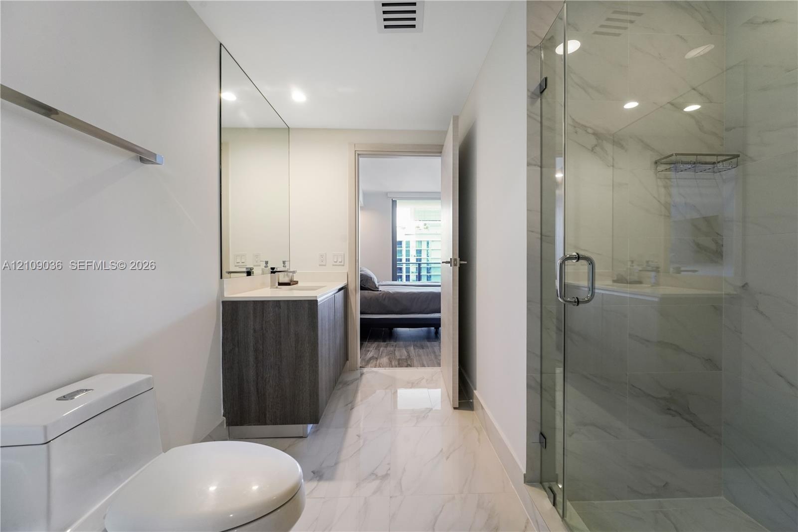 Bathroom featuring a dark wood-finish vanity, light-toned stone-style tile flooring, floor-to-ceiling vanity mirror, and a glass-enclosed shower with 