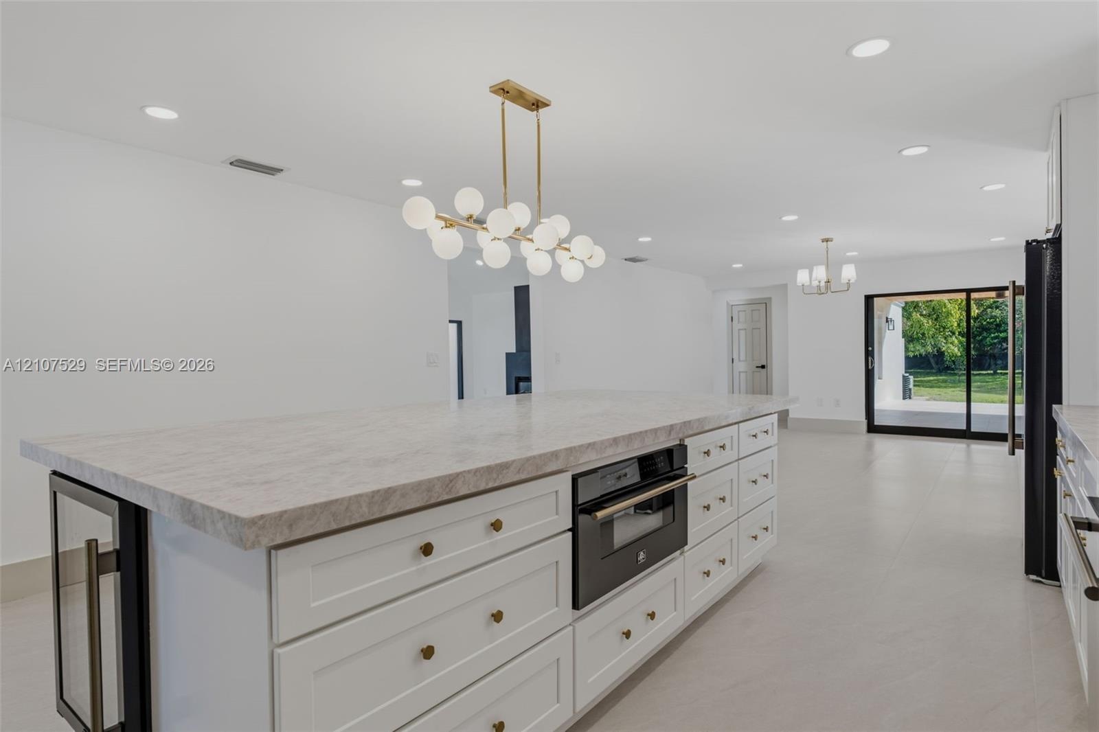 Kitchen featuring shaker-style cabinetry, stone countertops with matching backsplash, a large center island, built-in beverage refrigerator, and reces
