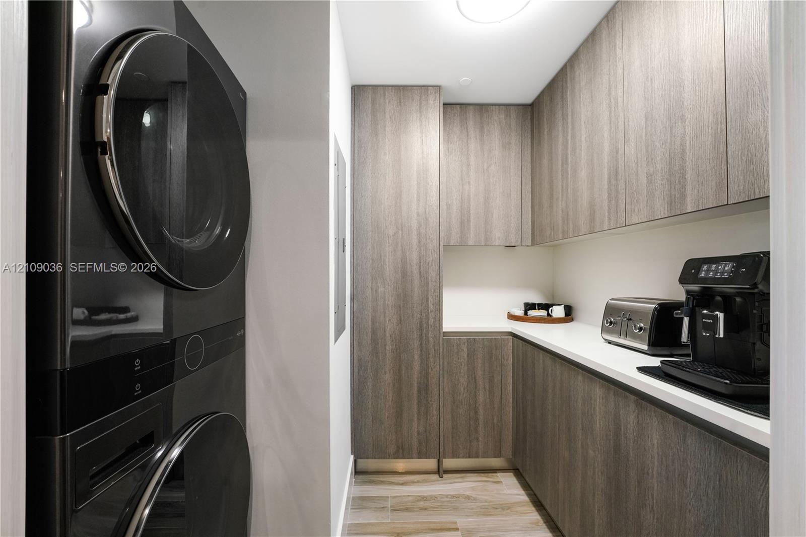 Utility room featuring stacked laundry appliances, wood-finish cabinetry, white solid-surface countertops, and wood-finish flooring