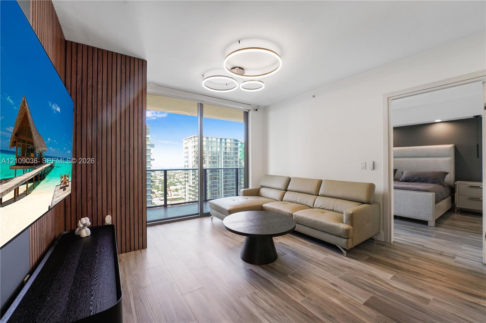 Vertical wood-slat accent wall, floor-to-ceiling glass windows, wood-finish flooring, and circular multi-ring LED flush-mount lighting