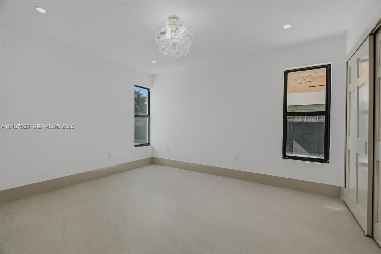 Neutral wall color, light-toned hard-surface flooring, black-framed windows, and a decorative tiered crystal chandelier