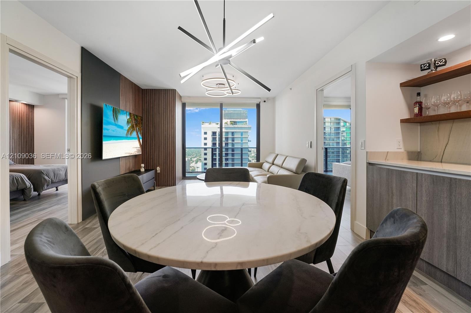 Modern living space featuring floor-to-ceiling windows, wood-panel accent wall, built-in wet bar with shelving, integrated recessed lighting, and a li