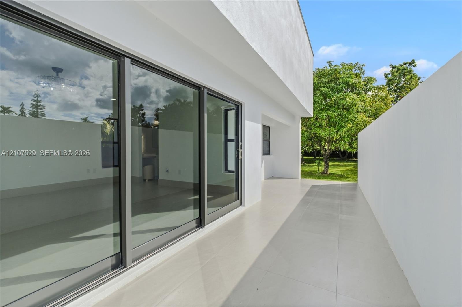 Modern exterior patio featuring smooth stucco walls, large-format tile flooring, oversized glass sliding doors, and dark-framed window casing