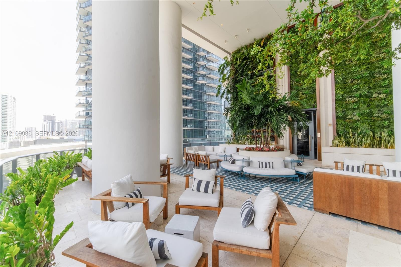 Covered terrace featuring stone tile flooring, a multi-story living wall, and large structural support columns