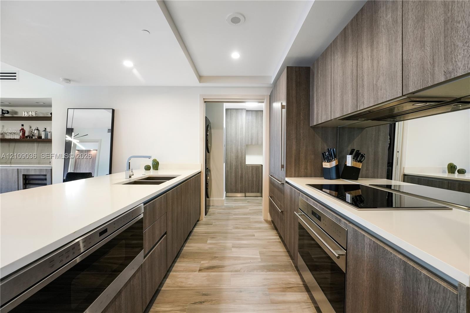 Modern kitchen featuring wood-finish cabinetry, white countertops, built-in stainless steel appliances, a mirrored backsplash, and wood-finish floorin
