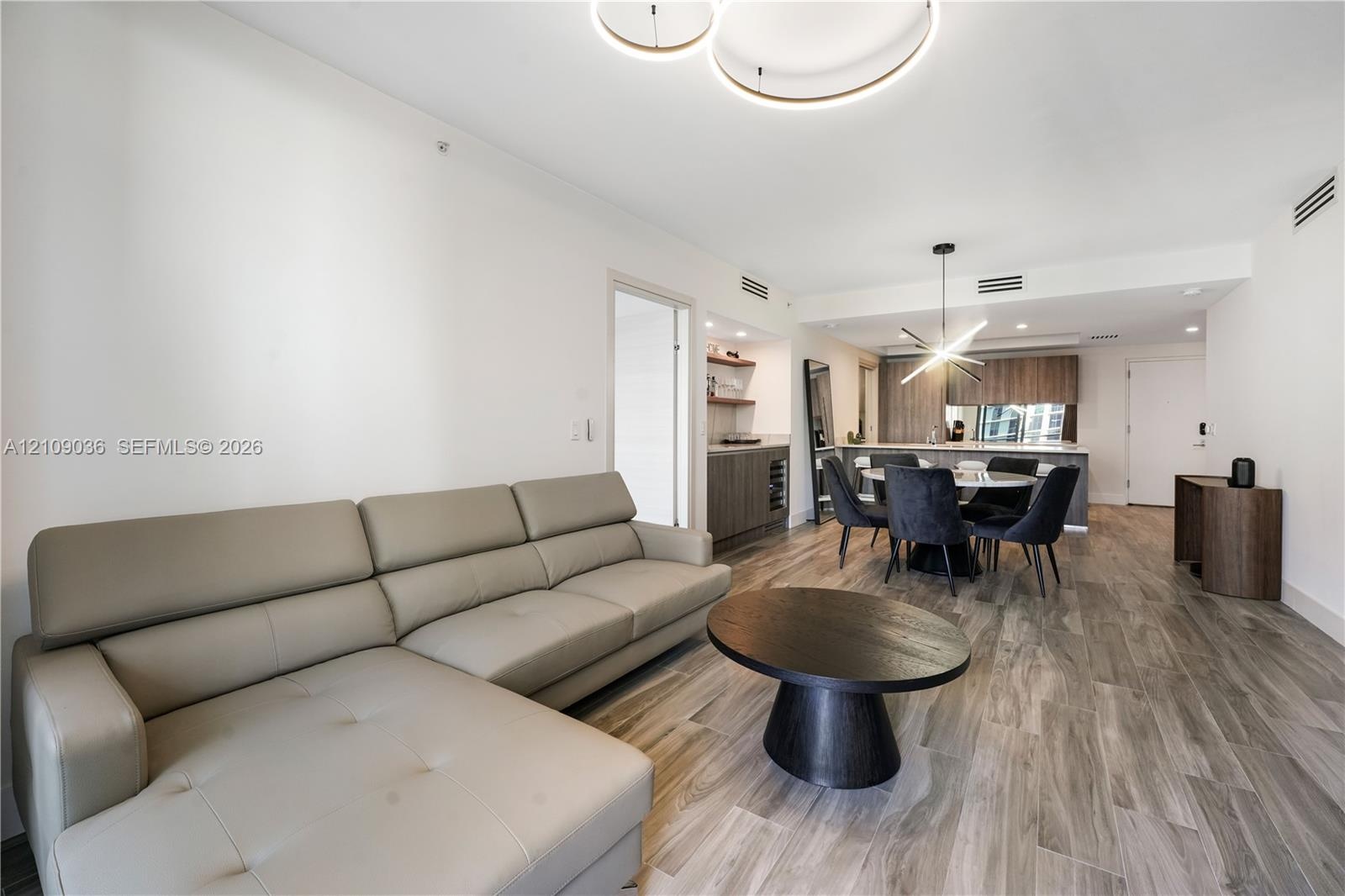 Open floor plan featuring wood-finish flooring, recessed lighting, modern circular halo chandelier, built-in wet bar with cabinetry, and kitchen with 