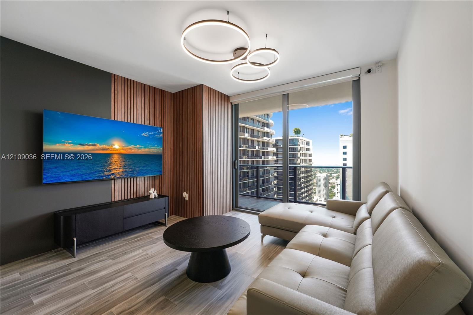 Living space featuring wood-finish flooring, floor-to-ceiling windows, modern multi-ring pendant lighting, and decorative wood-slat wall paneling