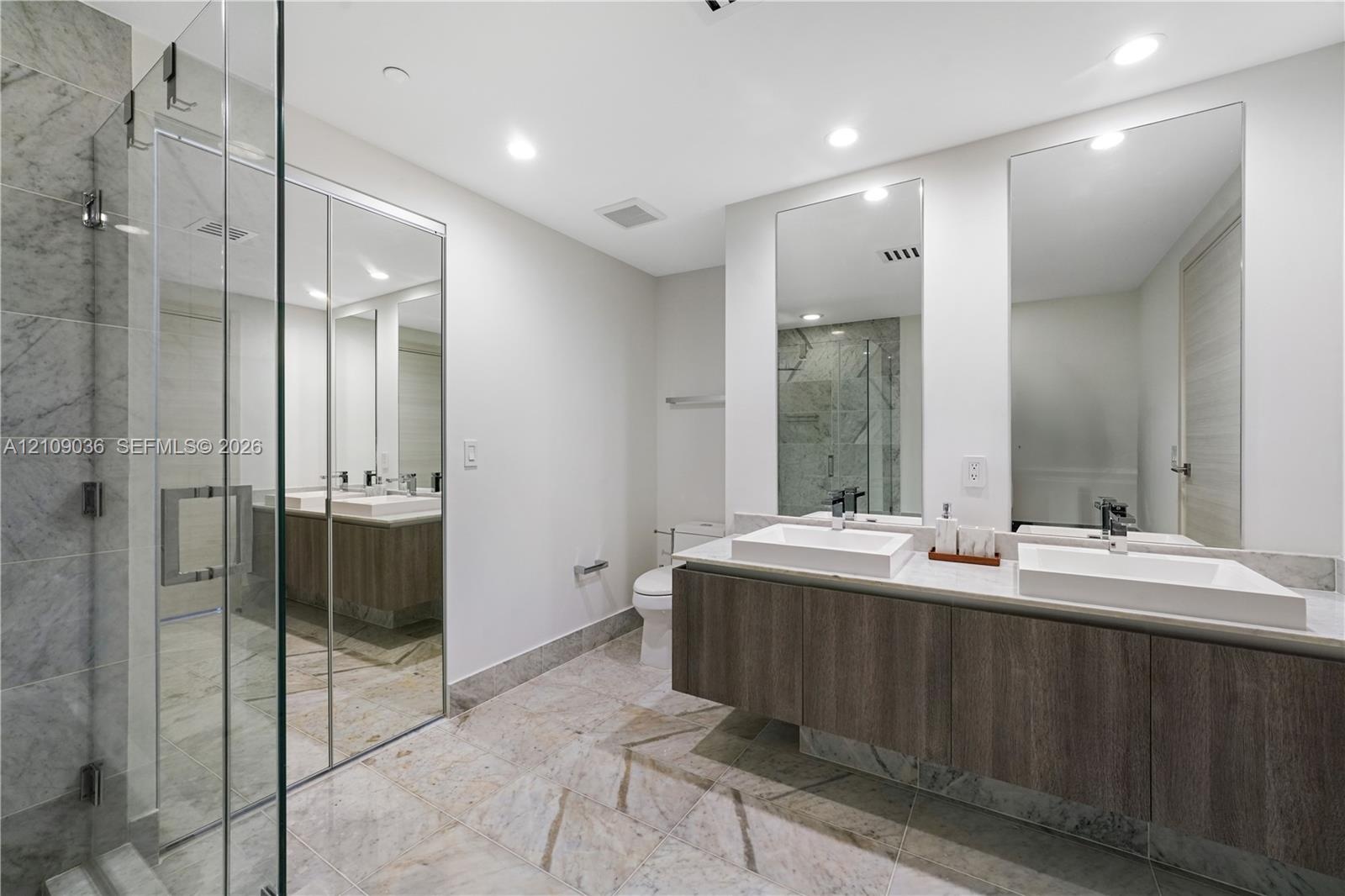 Floating double vanity with rectangular vessel sinks, floor-to-ceiling tiled glass-enclosed shower, stone-finish flooring, and dual wall-mounted mirro