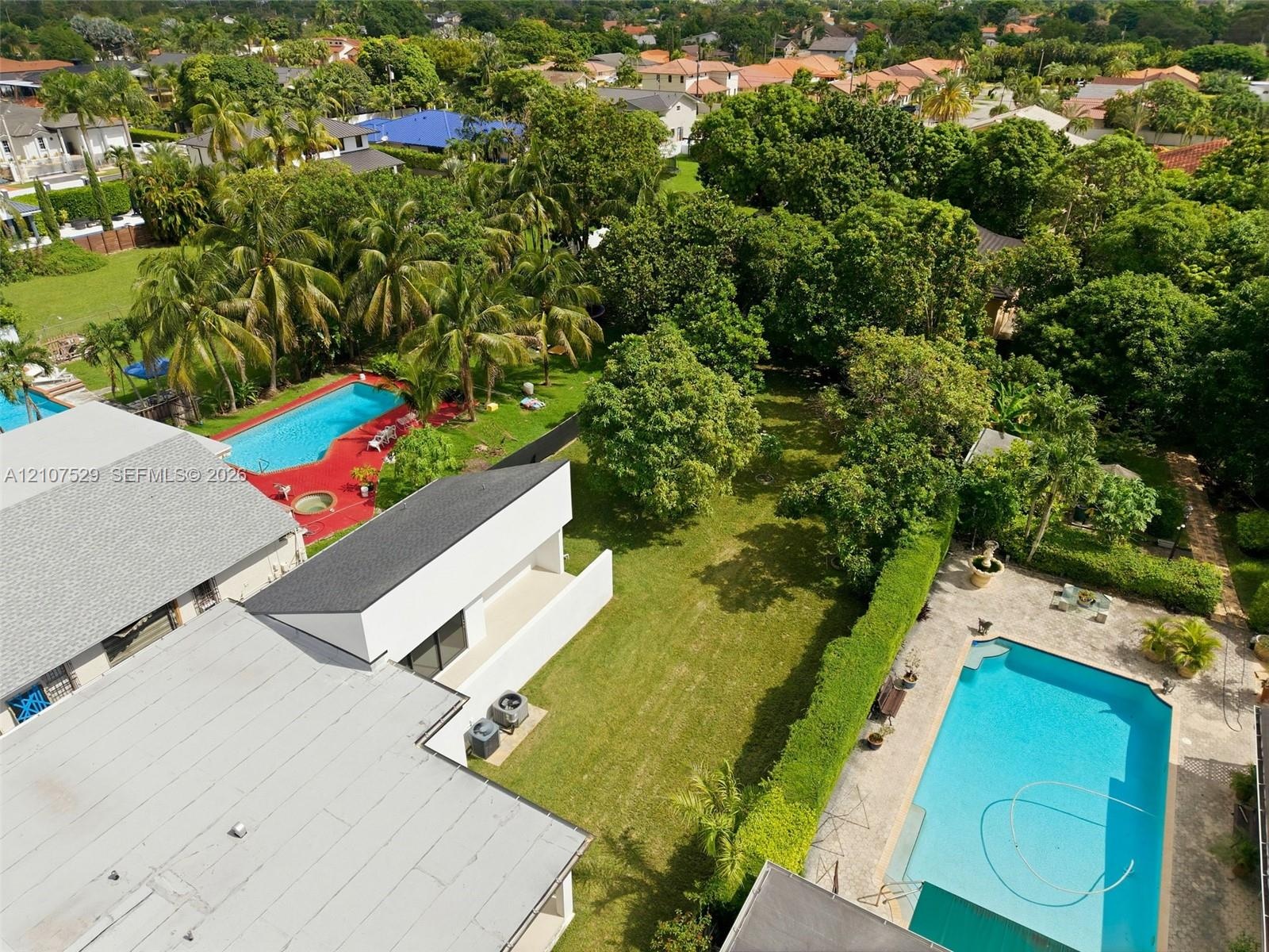Aerial perspective of a multi-section residential structure featuring a shingle roof and a spacious backyard with mature landscaping