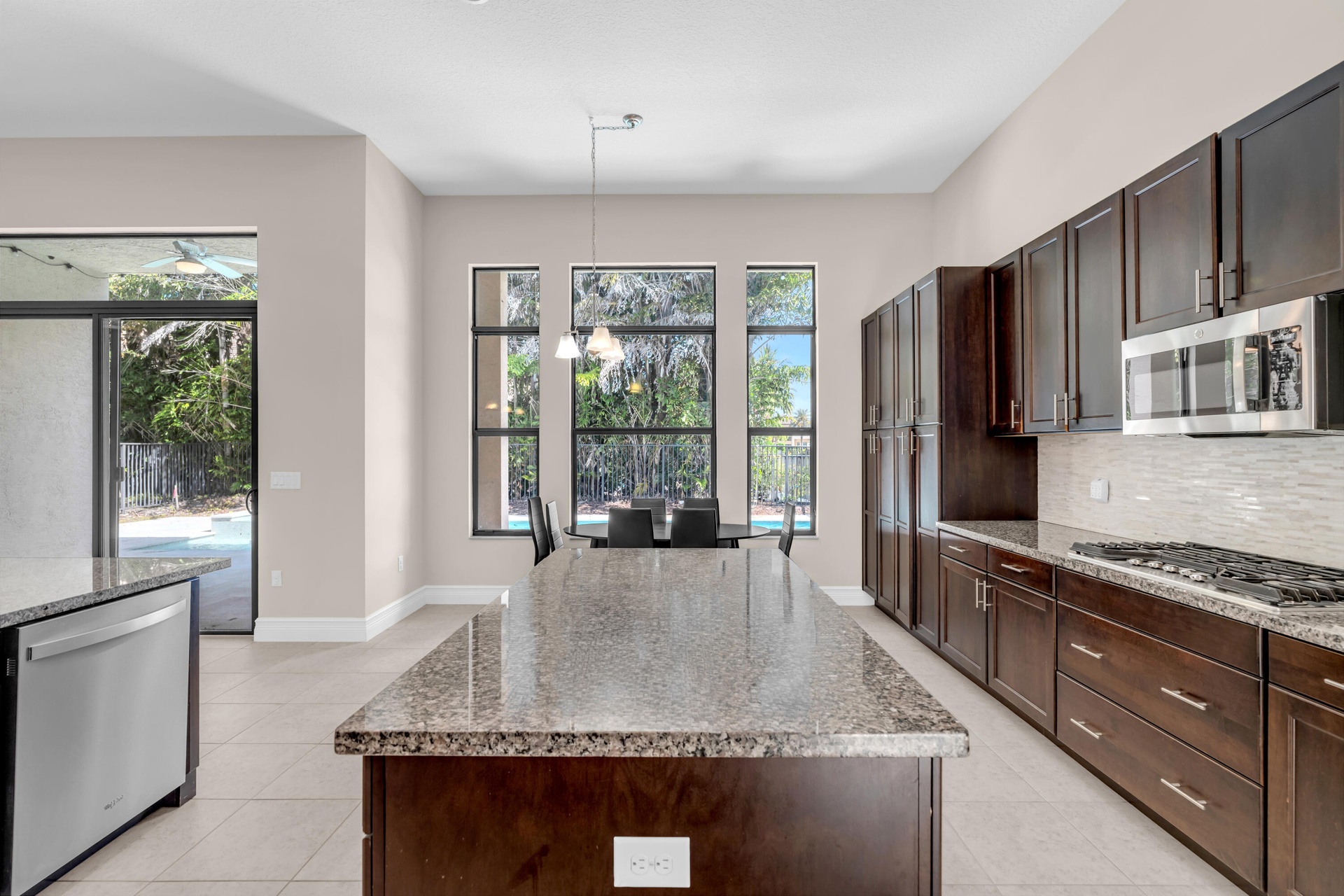 Gourmet kitchen featuring rich wood cabinetry, stainless steel appliances including a built-in microwave, granite countertops, and a substantial cente