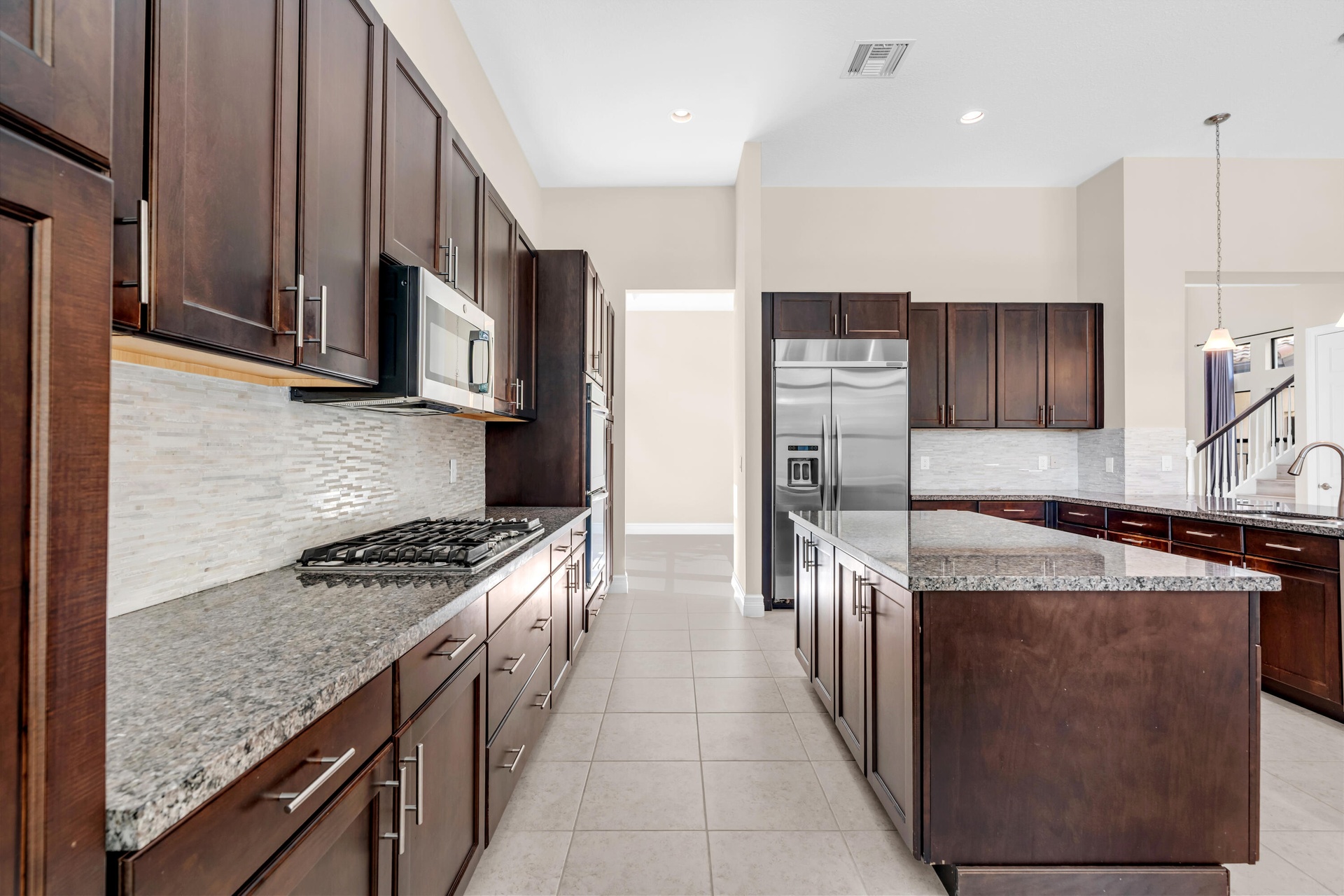 Kitchen featuring dark wood cabinetry, light granite countertops, a gas range, a mosaic tile backsplash, and stainless steel appliances