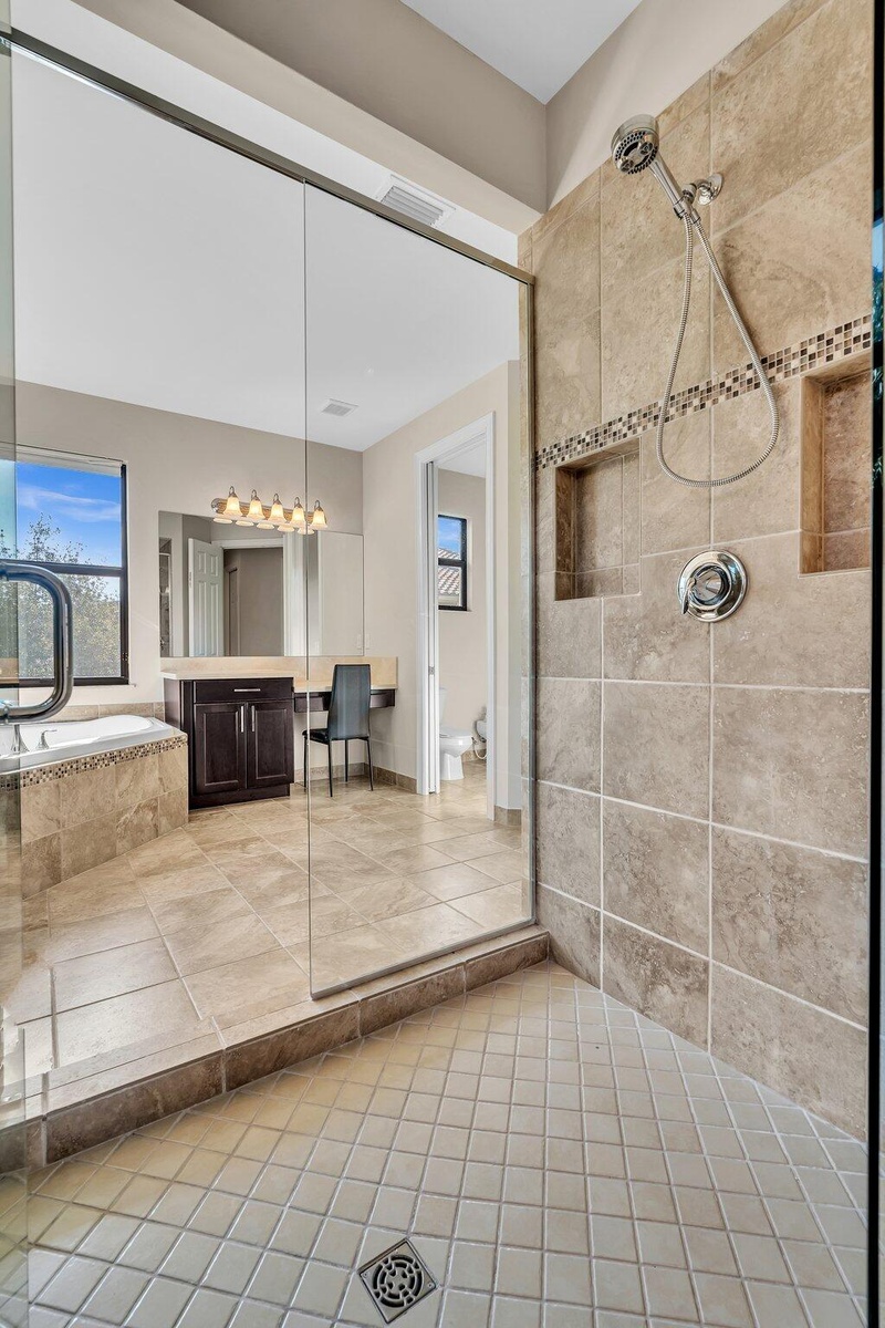 Glass-enclosed shower featuring large format wall tiles with a decorative mosaic accent and dual recessed niches
