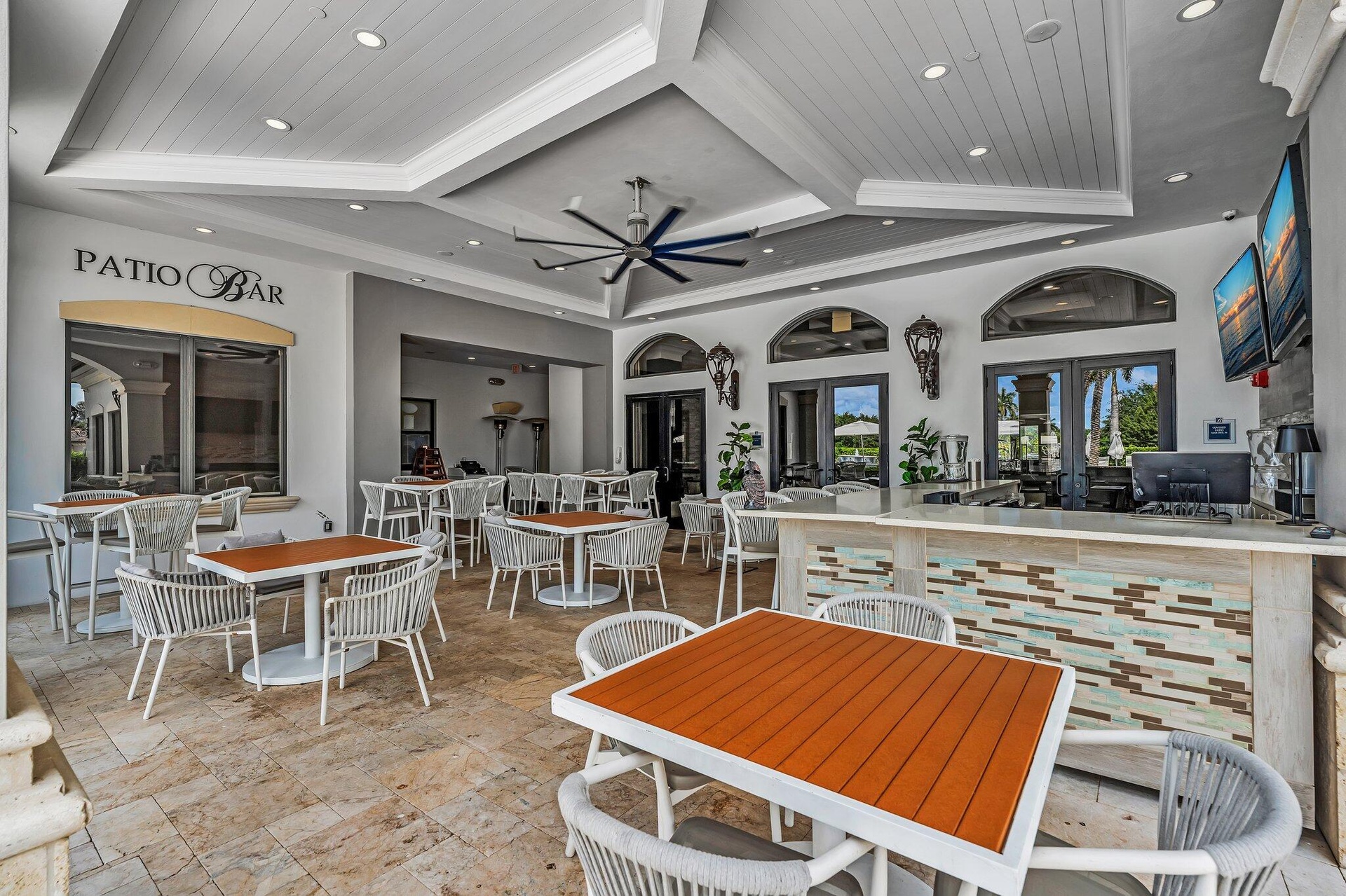 Spacious outdoor patio area featuring a textured tile floor, a built-in bar with a stone countertop and decorative wood-finish paneling, a detailed tr