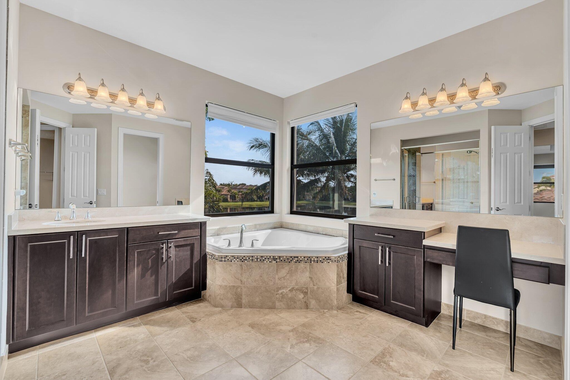 Spacious bathroom featuring a corner soaking tub, dual dark wood vanities with light countertops, a separate vanity area, large mirrors, and tile floo