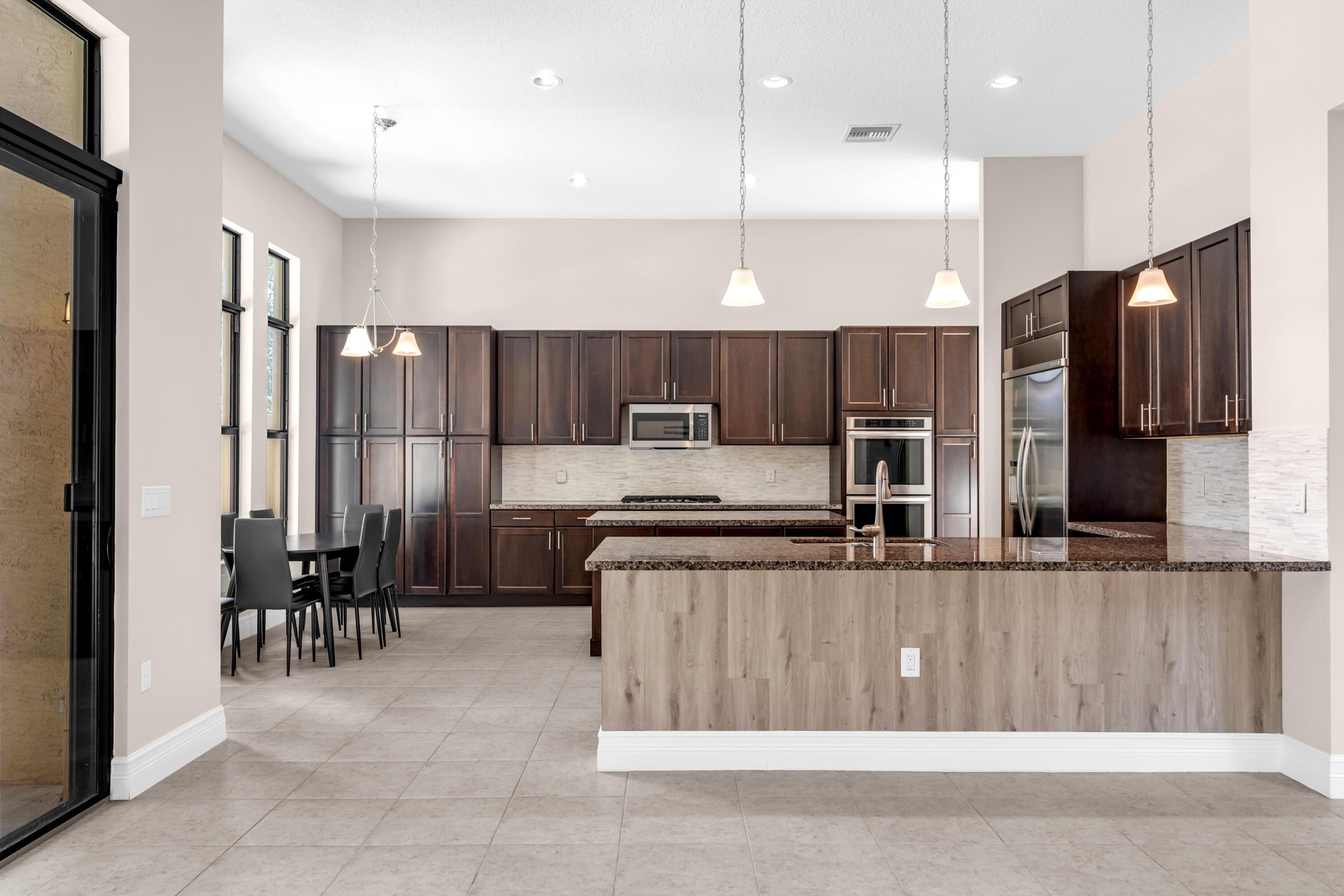 Open-concept kitchen and dining area featuring dark wood cabinetry, stainless steel appliances, a large island with wood-finish base, pendant lighting