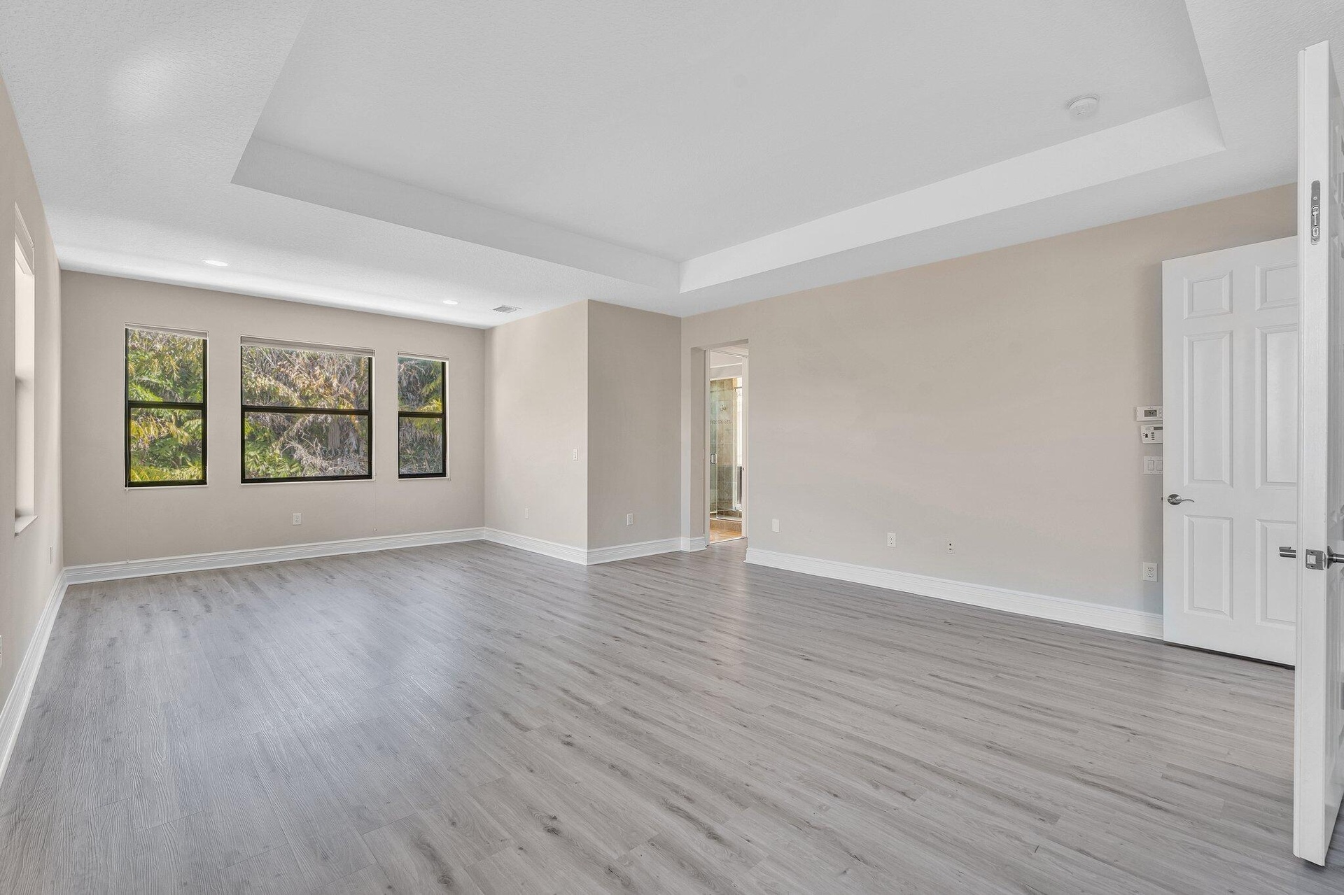 Spacious living area showcasing gleaming wood-finish flooring, a coffered ceiling with recessed lighting, and abundant natural light from triple-pane 