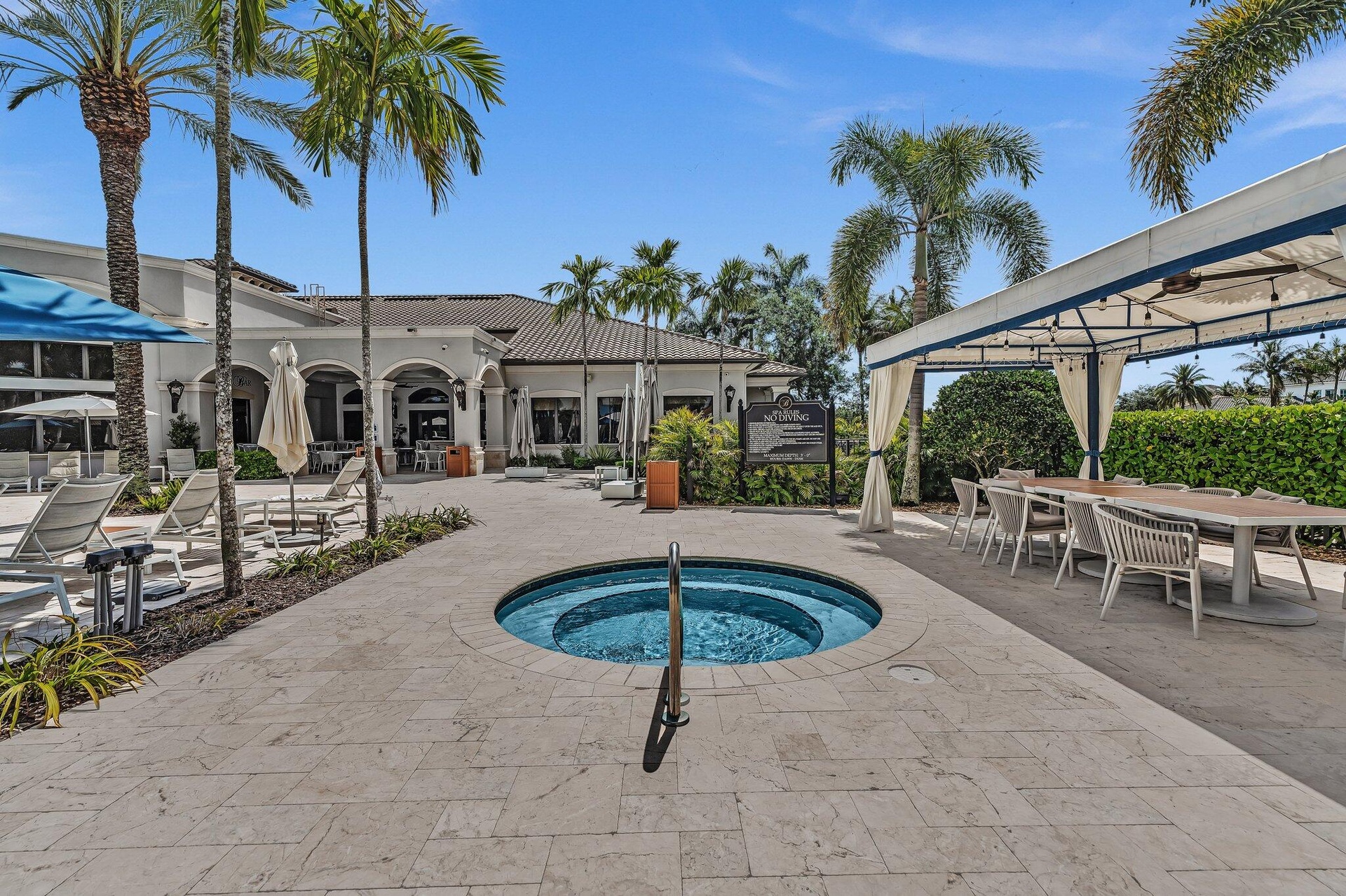 Resort-style outdoor entertaining space featuring a circular spa with integrated seating, expansive paved terrace, mature palm trees, pergola-covered 