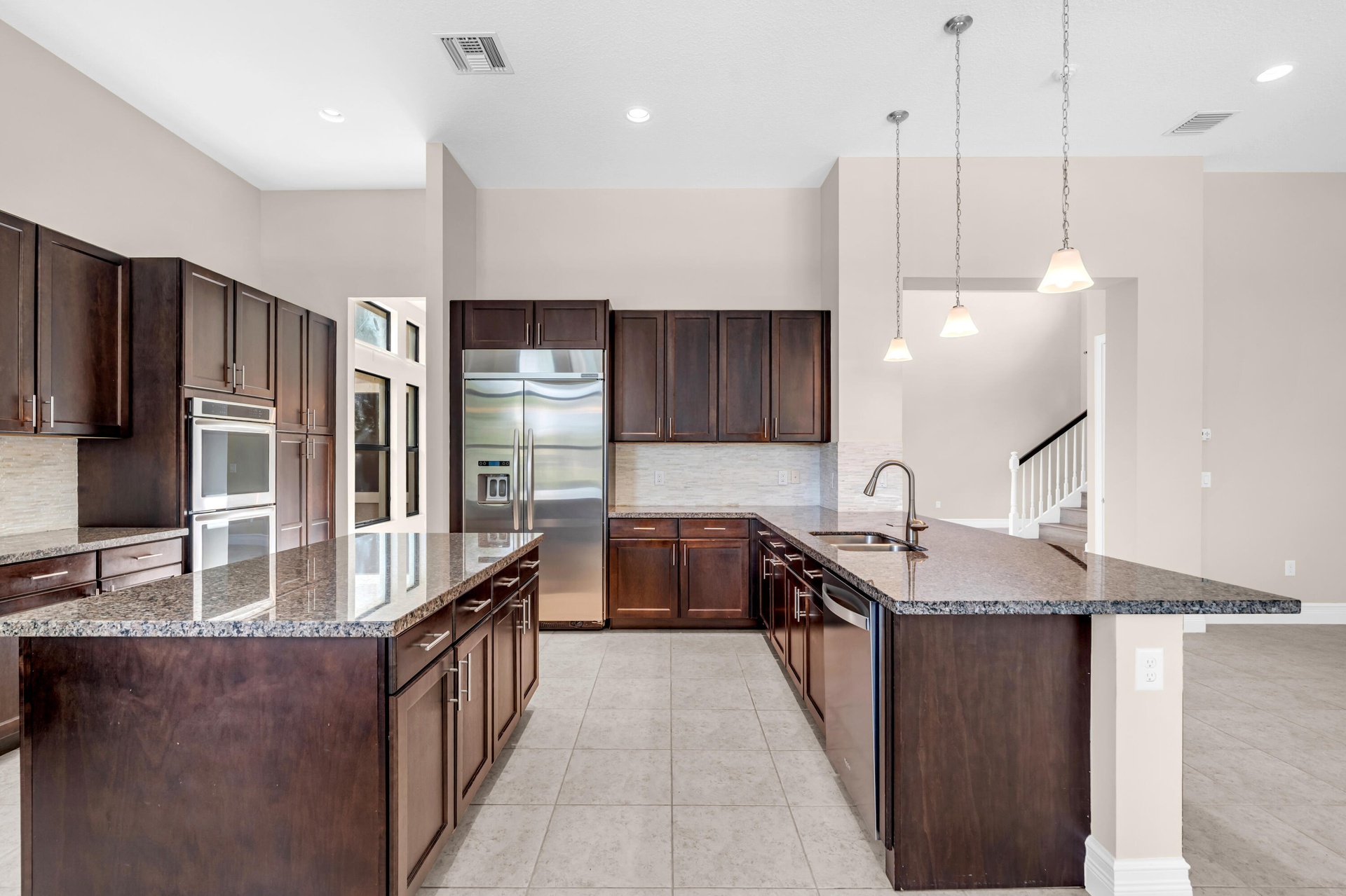 Expansive kitchen featuring dual islands with granite countertops, rich wood cabinetry, stainless steel appliances, and tile flooring