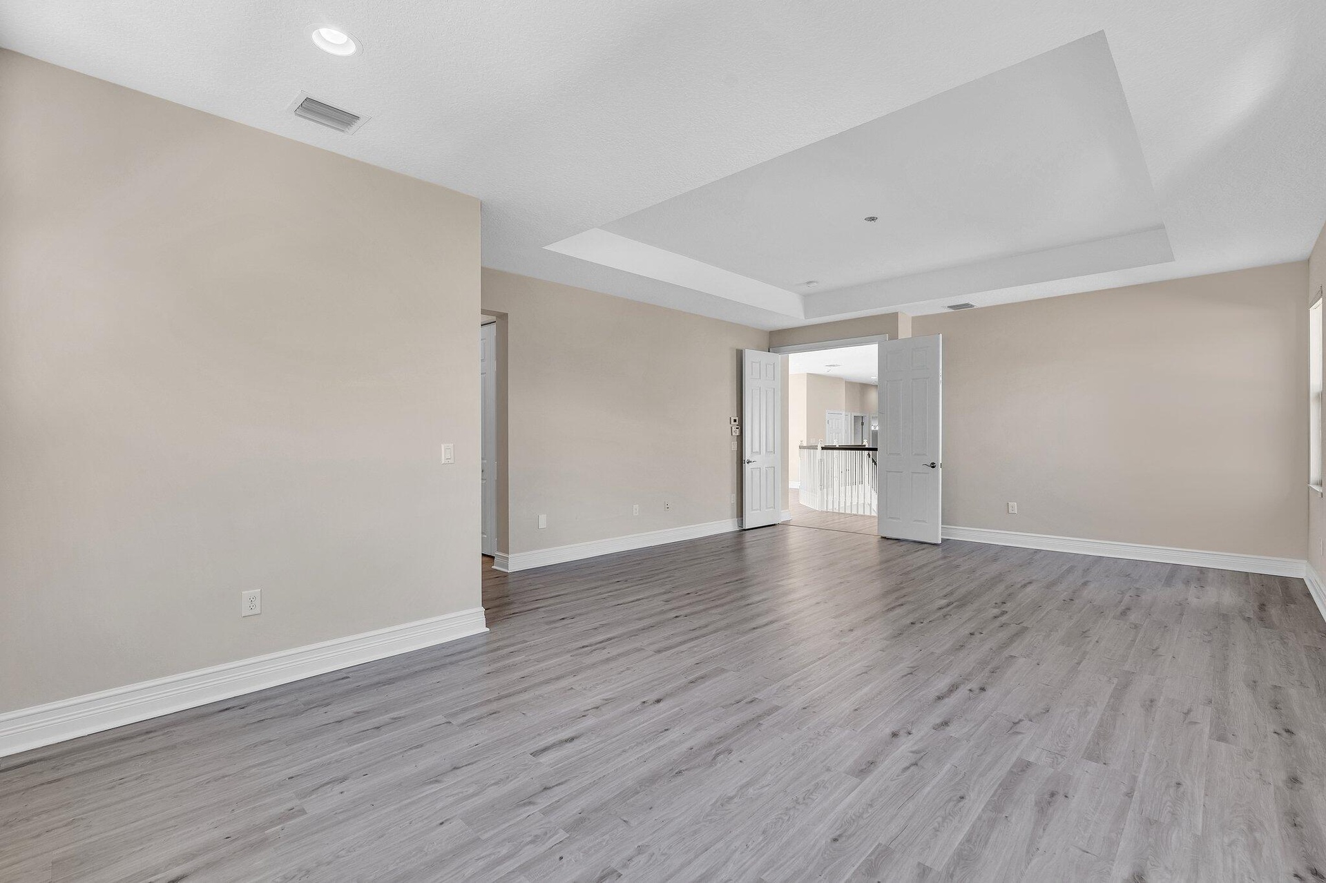 Spacious room featuring light gray wood-finish flooring, neutral wall tones, and a tray ceiling
