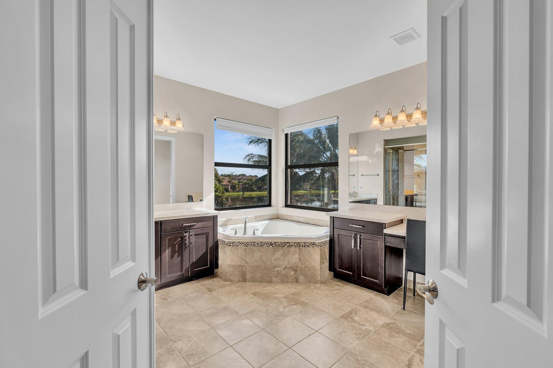 Expansive bathroom featuring a built-in corner soaking tub, dual vanity areas with dark wood cabinetry and light countertops, and large windows