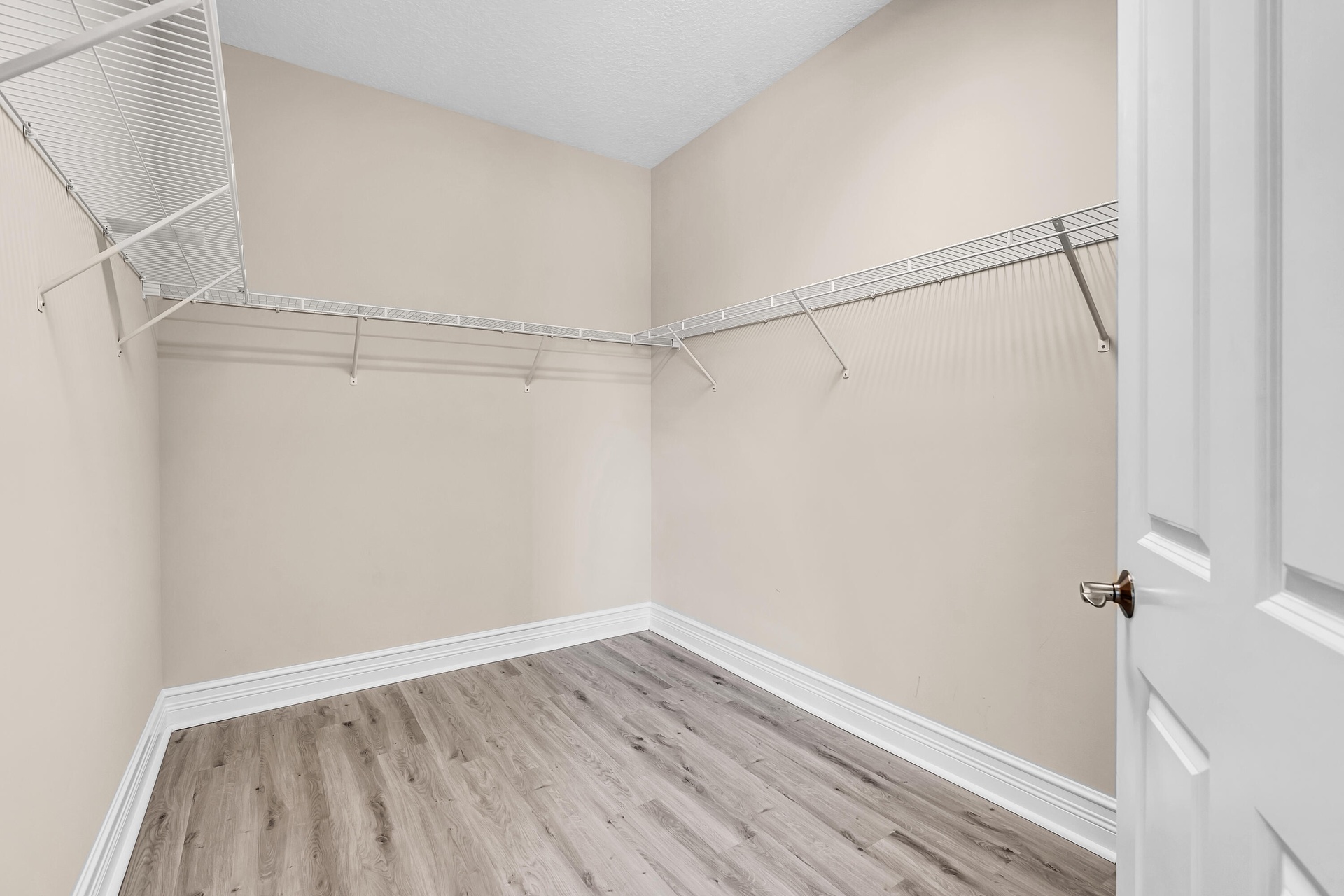 Interior closet featuring wood-finish flooring, white wire shelving, baseboard molding, and a paneled door