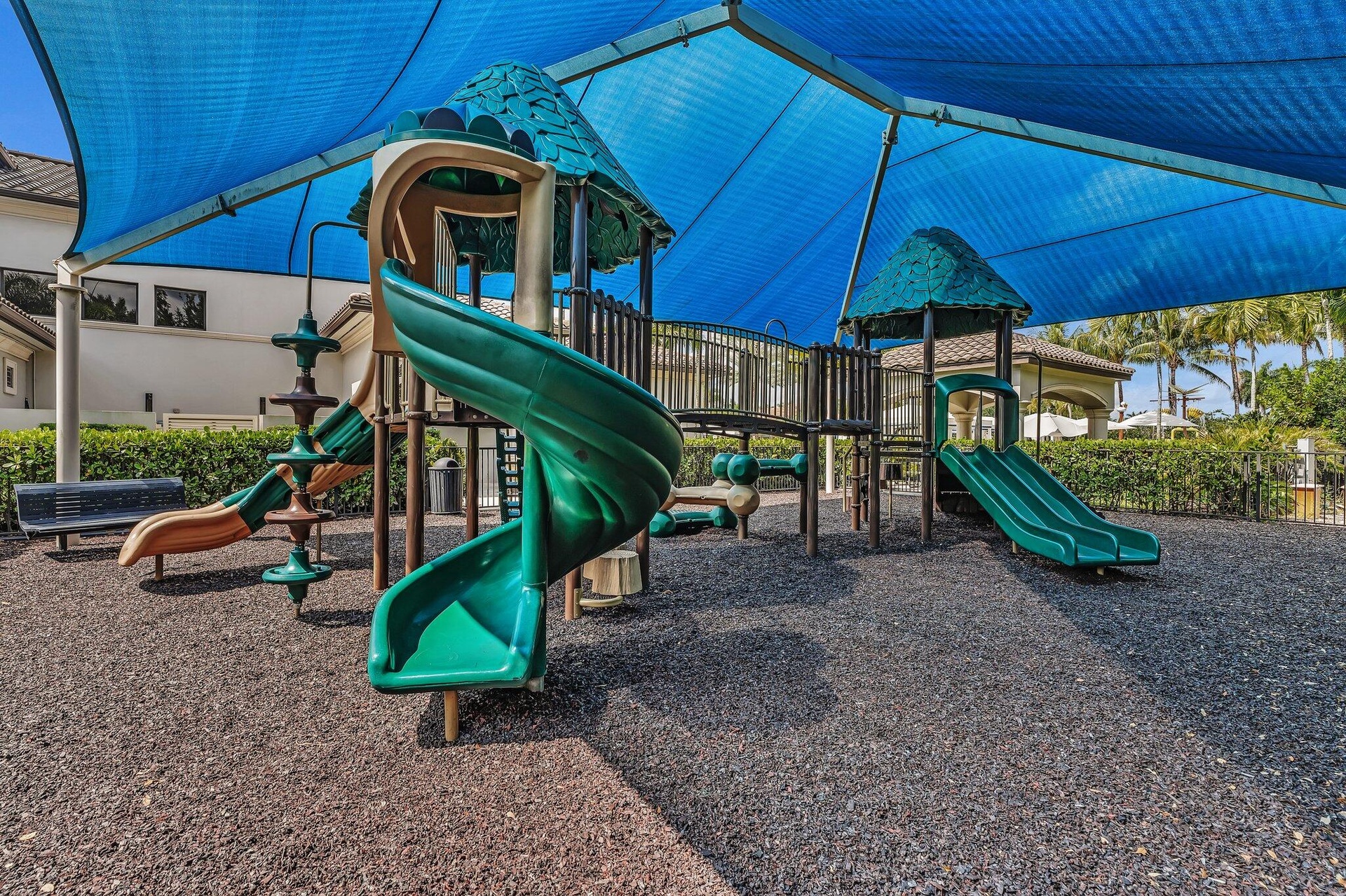 Expansive recreational area featuring dual spiral tube slides with elevated platforms, ground-level play structures, and engineered wood-fiber surfaci