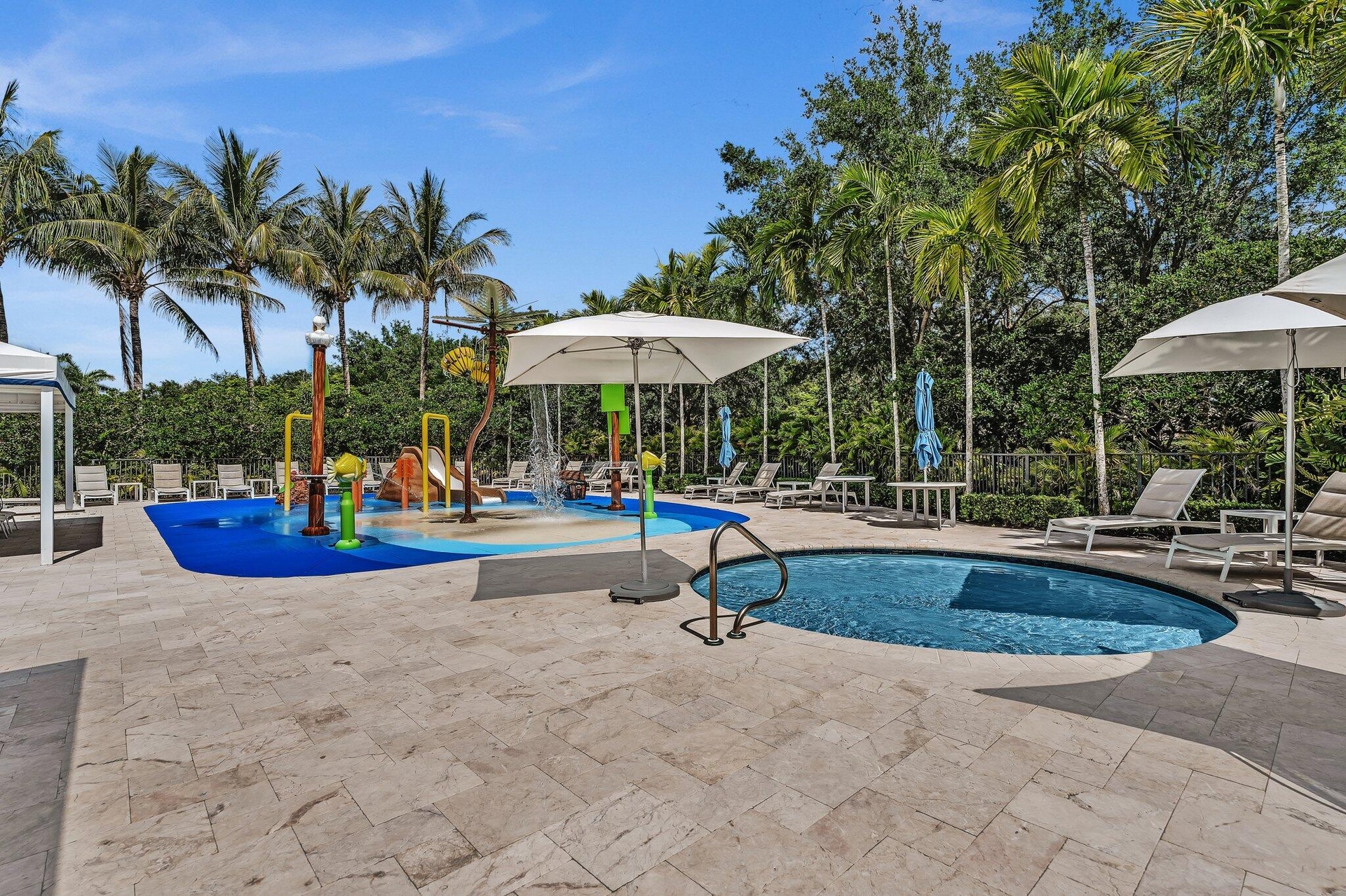 Outdoor amenity area featuring a splash pad with various water features, a circular spa with metal handrail, and multiple lounge chairs