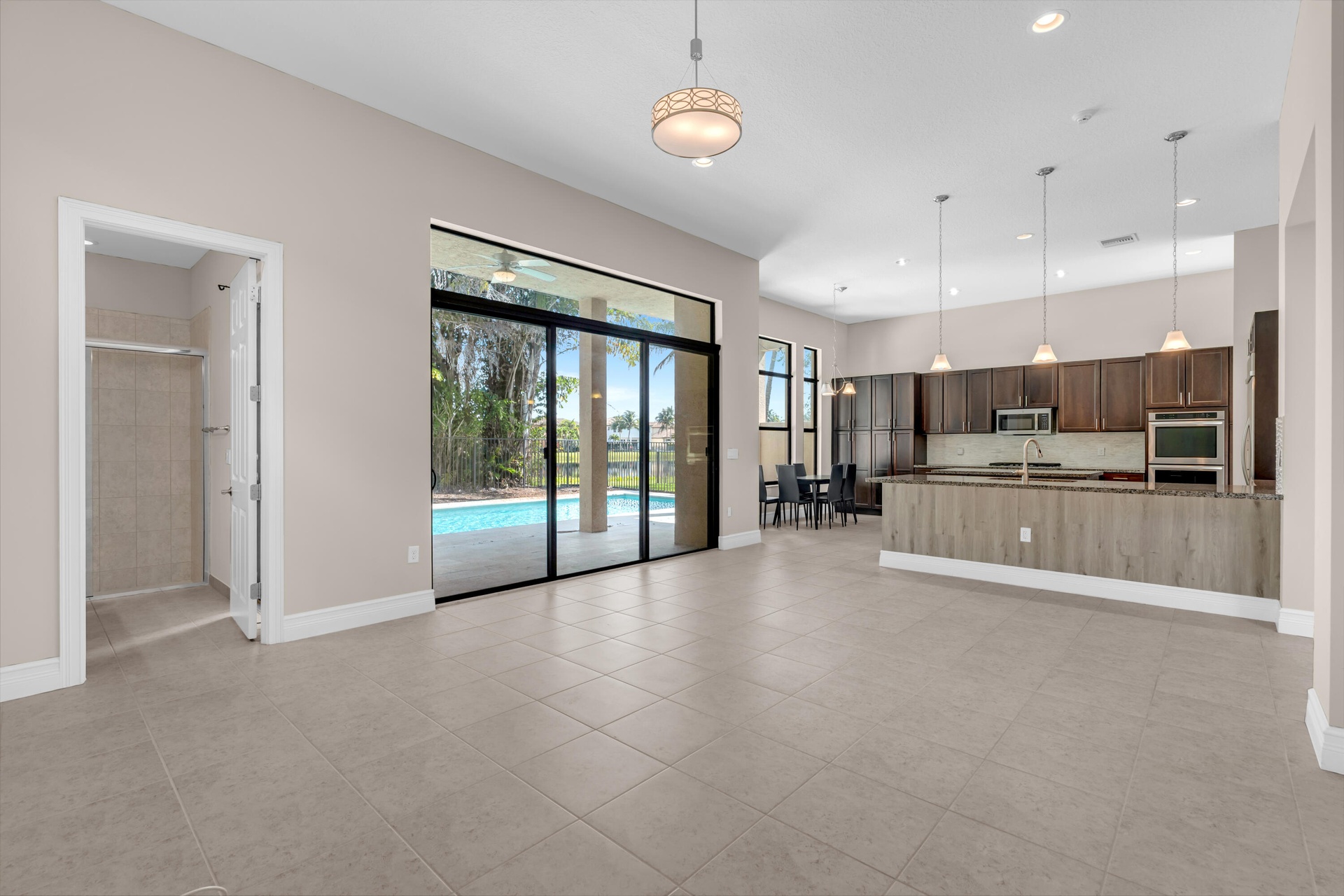 Spacious open-concept living area featuring polished tile flooring, recessed ceiling lighting, and a wood-finish kitchen with integrated appliances