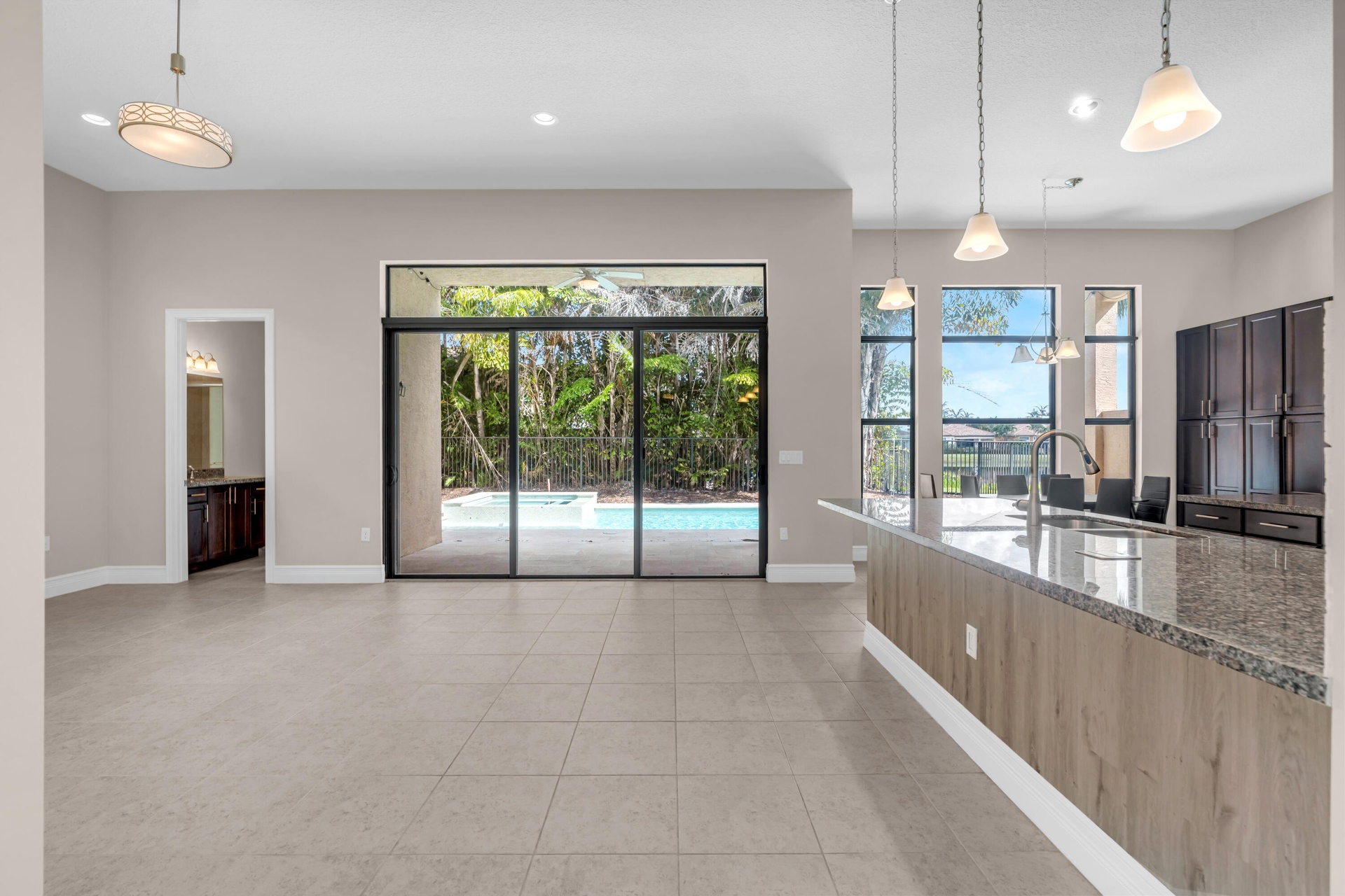 Open-concept living space featuring expansive tile flooring, pendant lighting, and abundant natural light from floor-to-ceiling sliding glass doors an