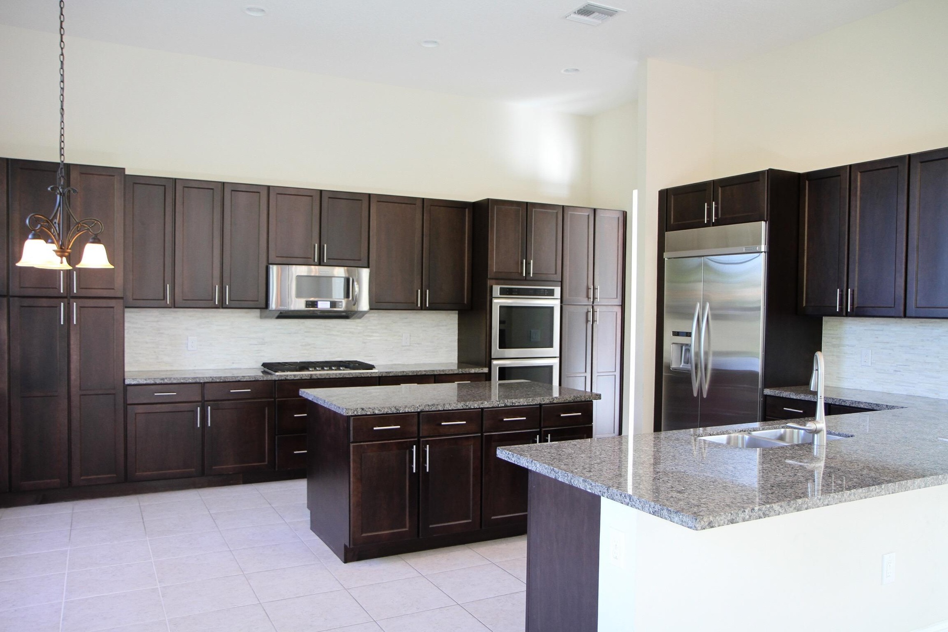 Kitchen featuring dark wood cabinetry, light-toned tile flooring, stainless steel appliances, granite countertops, and a central island