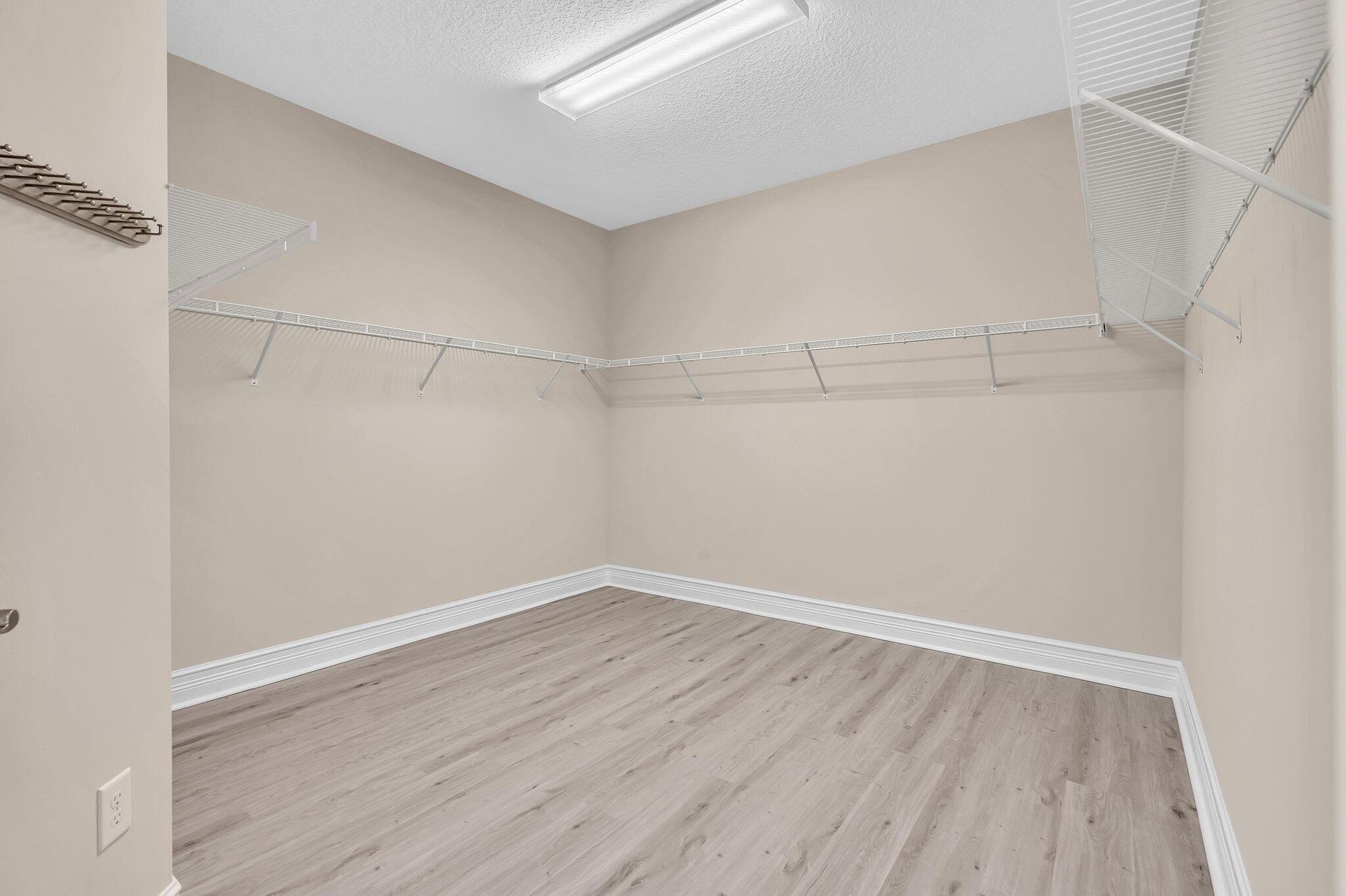 Spacious walk-in closet featuring pristine wood-finish flooring, neutral painted walls, and extensive wire shelving systems throughout