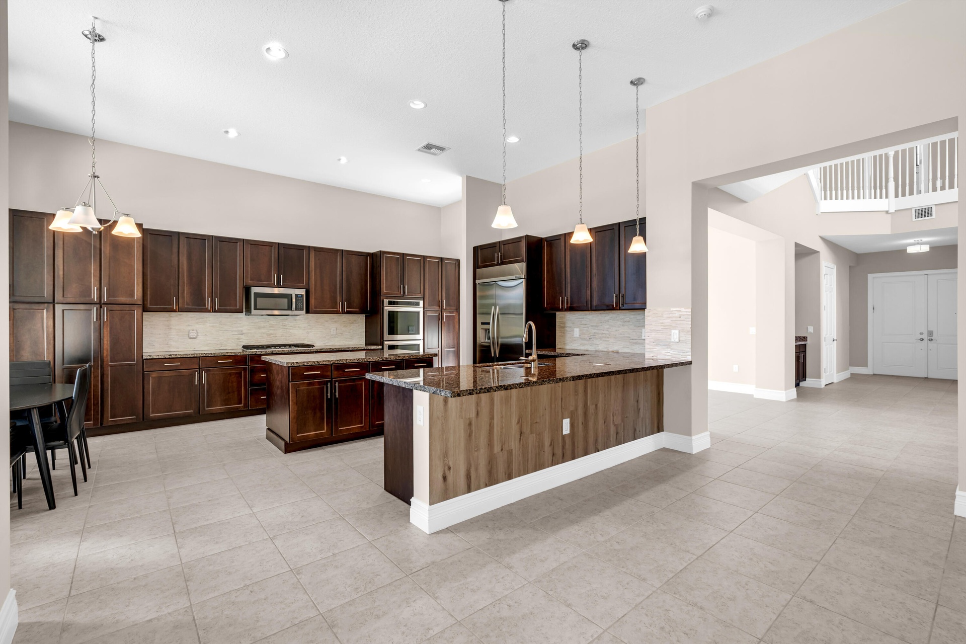 Spacious kitchen featuring dark wood cabinetry, a central island with a gas cooktop, double ovens, and a large breakfast bar with pendant lighting