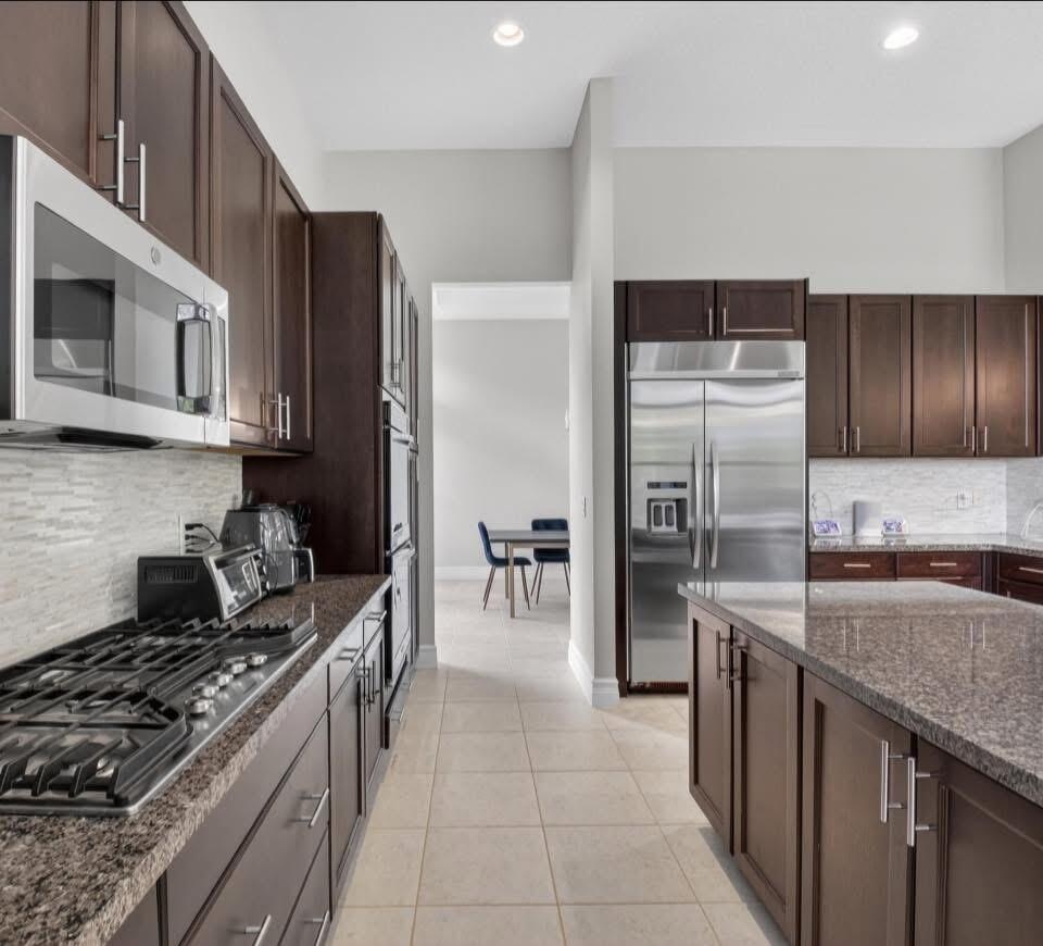 Galley-style kitchen featuring dark wood cabinetry, stainless steel appliances including a gas cooktop and side-by-side refrigerator, granite countert