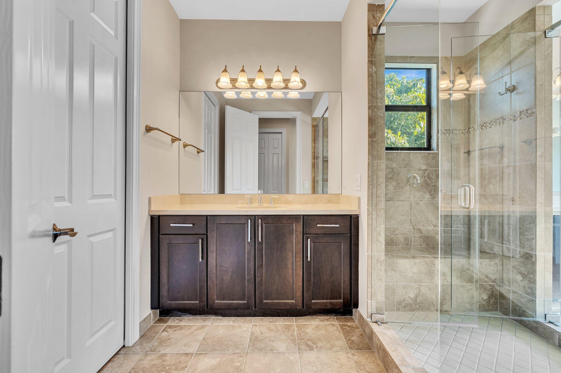 Spa-inspired primary bathroom featuring a dark wood vanity with multiple storage cabinets, marble-look countertops, and brass hardware